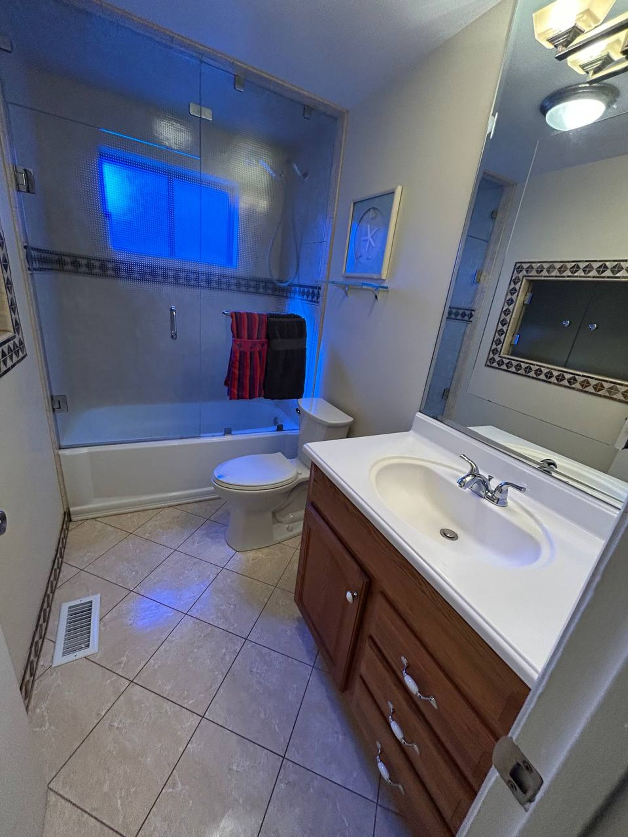 Bathroom with glass tub enclosure, white sink top and beige floor tile