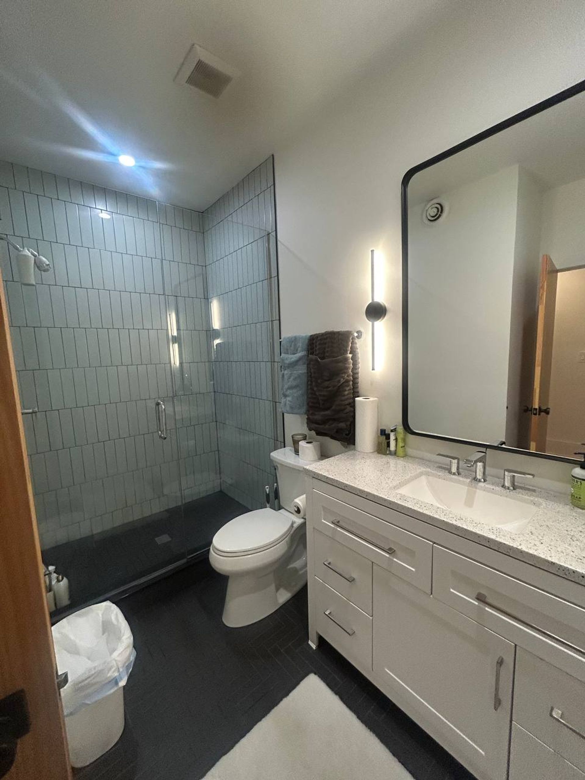 Bathroom with glass walk-in shower, green-gray tile and white vanity