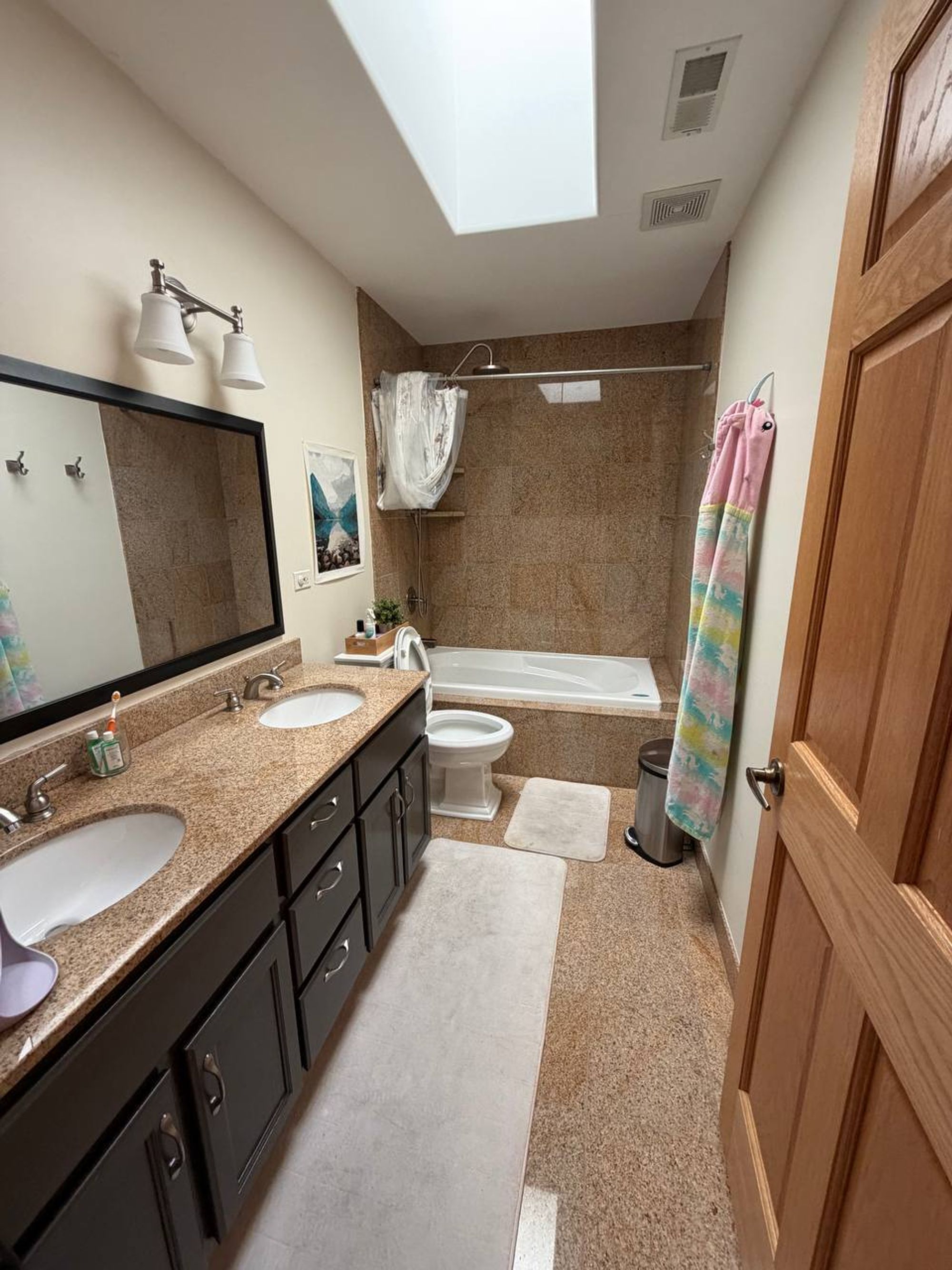 Bathroom with skylight, granite double vanity and tub with stone tile