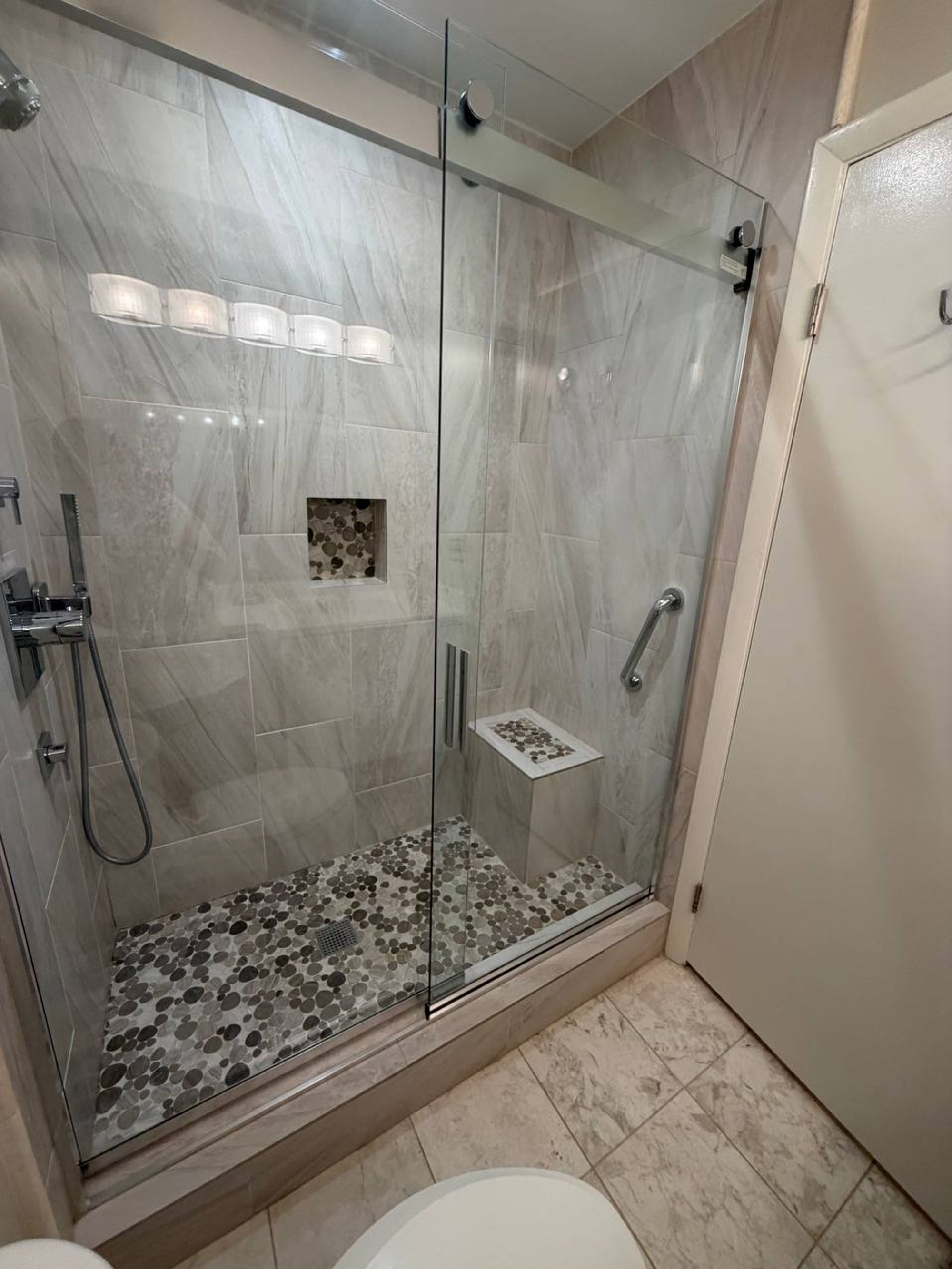 Glass walk-in shower with gray tile walls and pebble stone floor