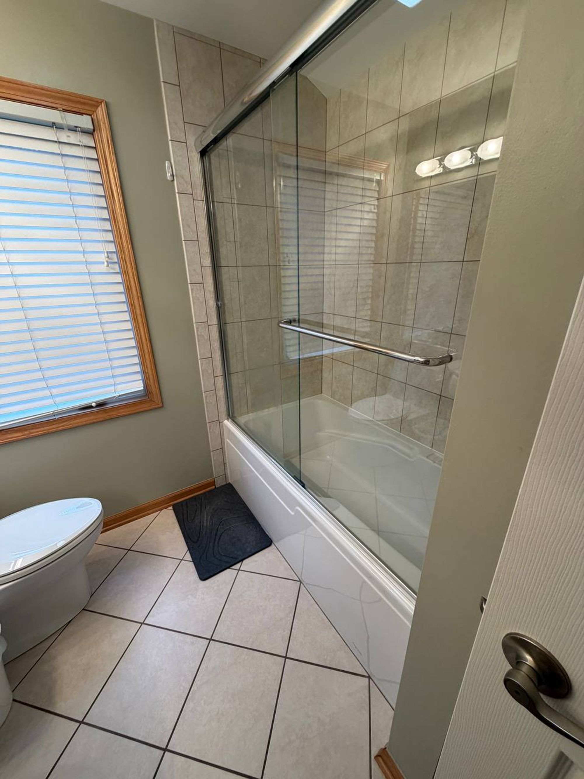 Tub with sliding glass doors next to a window with blinds