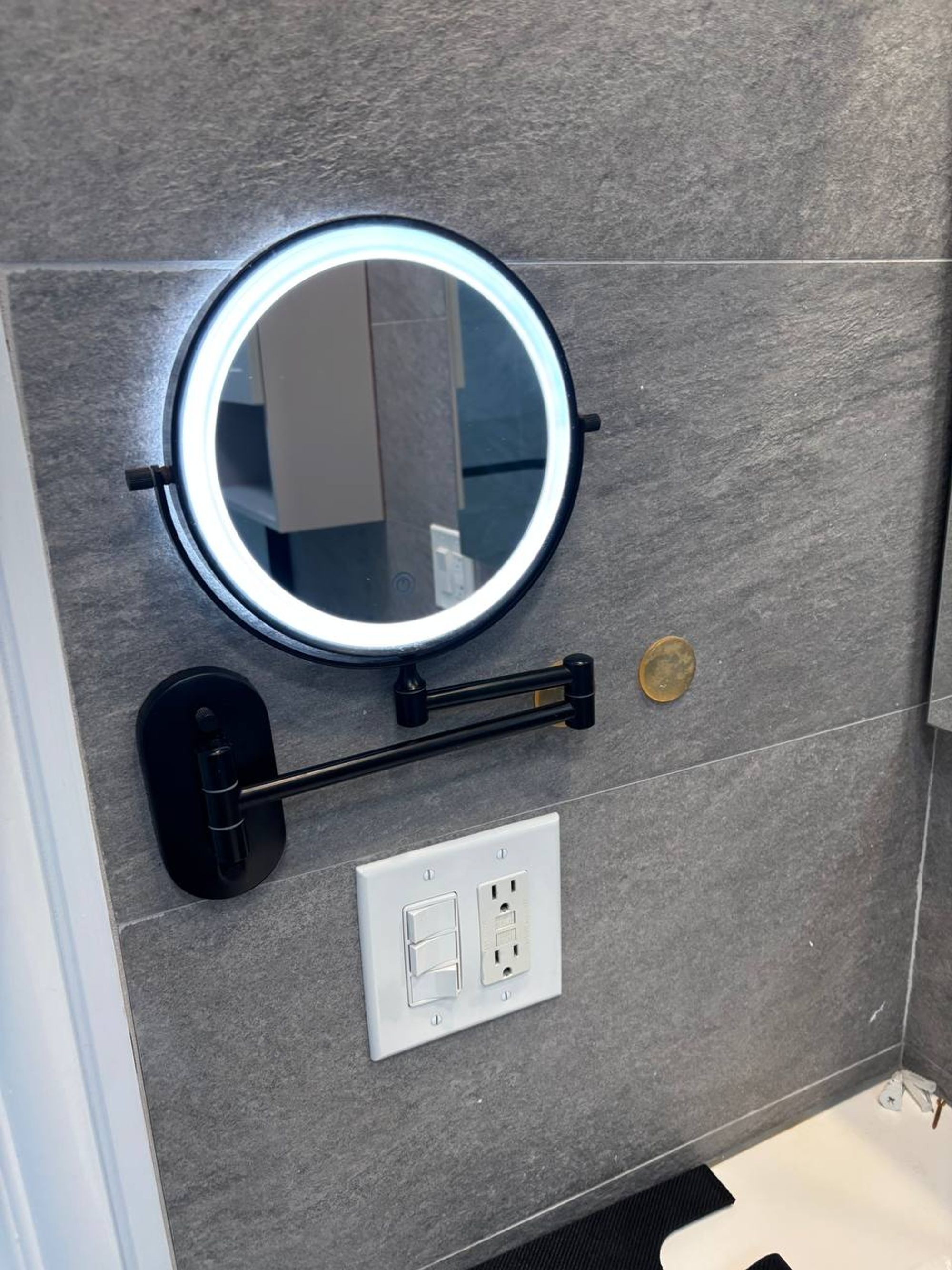 Lighted round makeup mirror on gray tile bathroom wall
