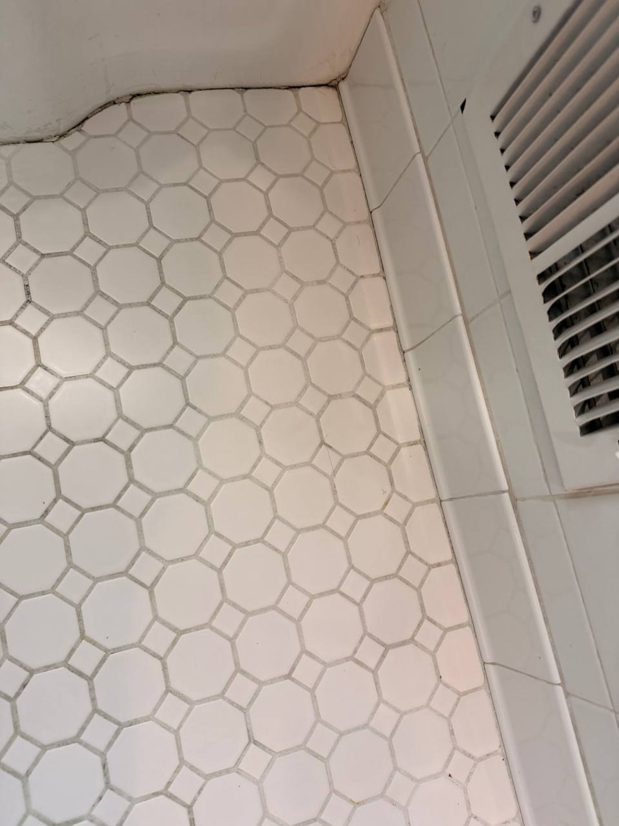 White octagon floor tile with clean grout along the wall