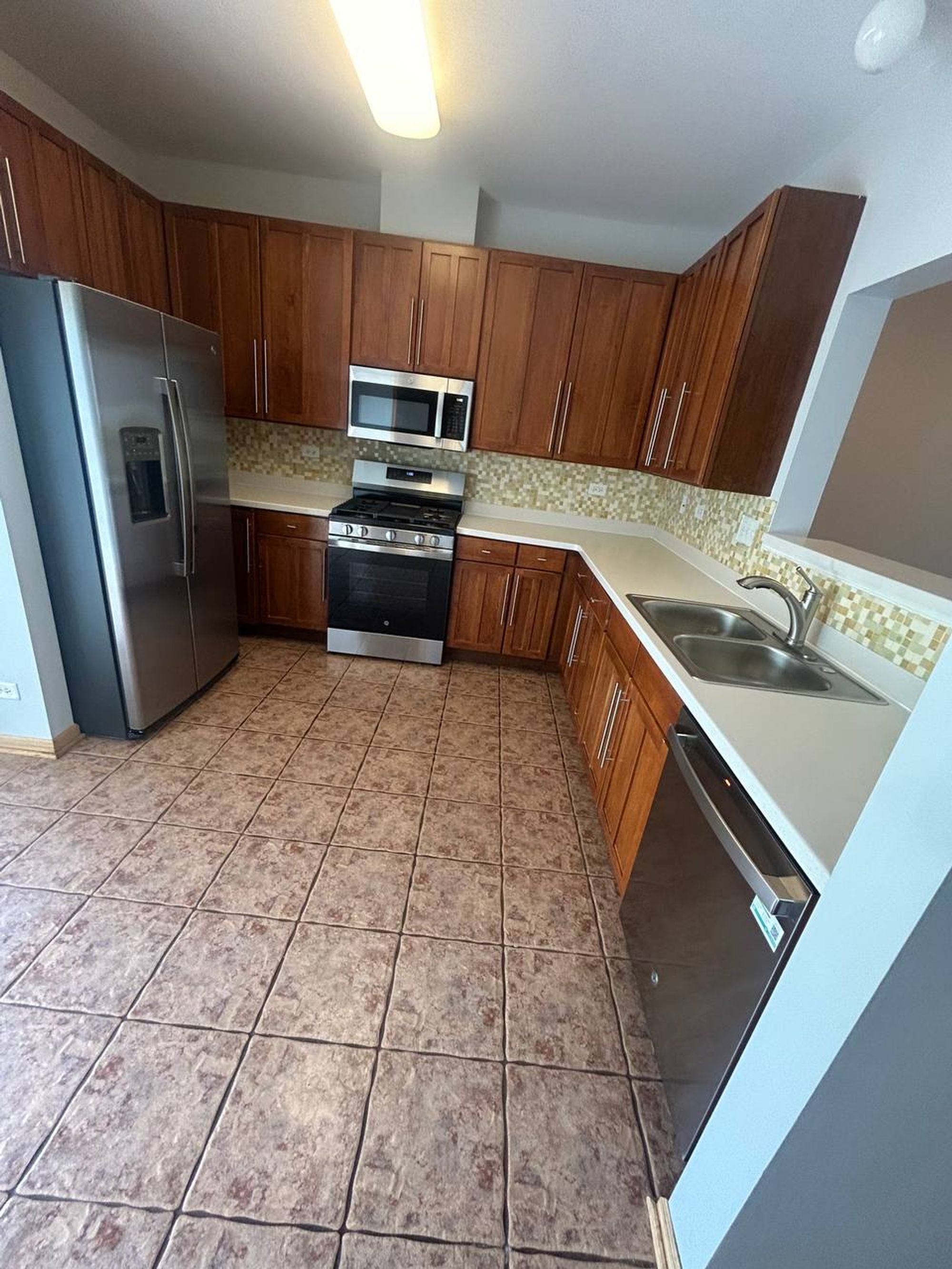 Empty kitchen with wood cabinets, steel appliances and tile floor