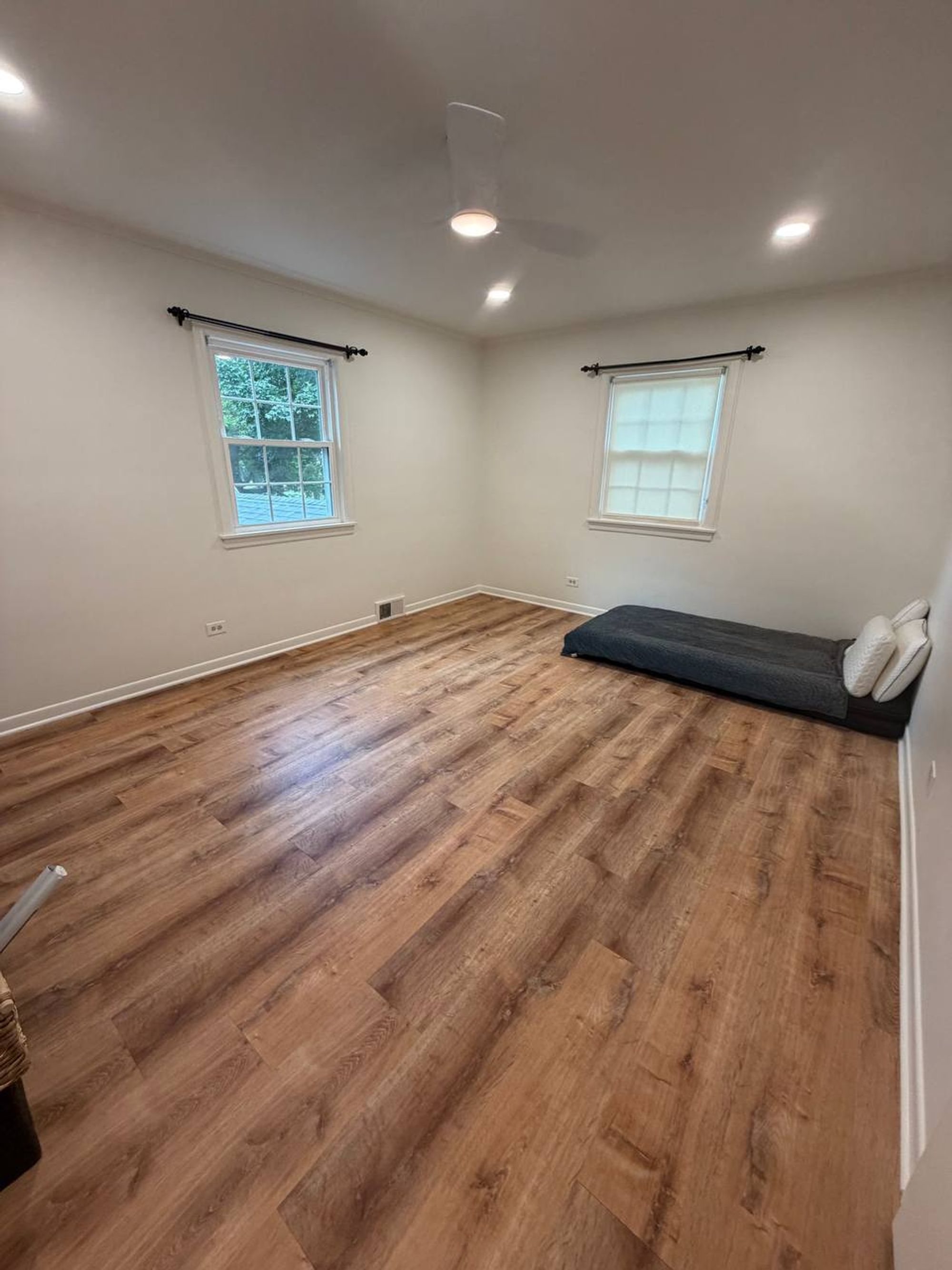 Large bedroom with ceiling fan, two windows and clean wood-look floor