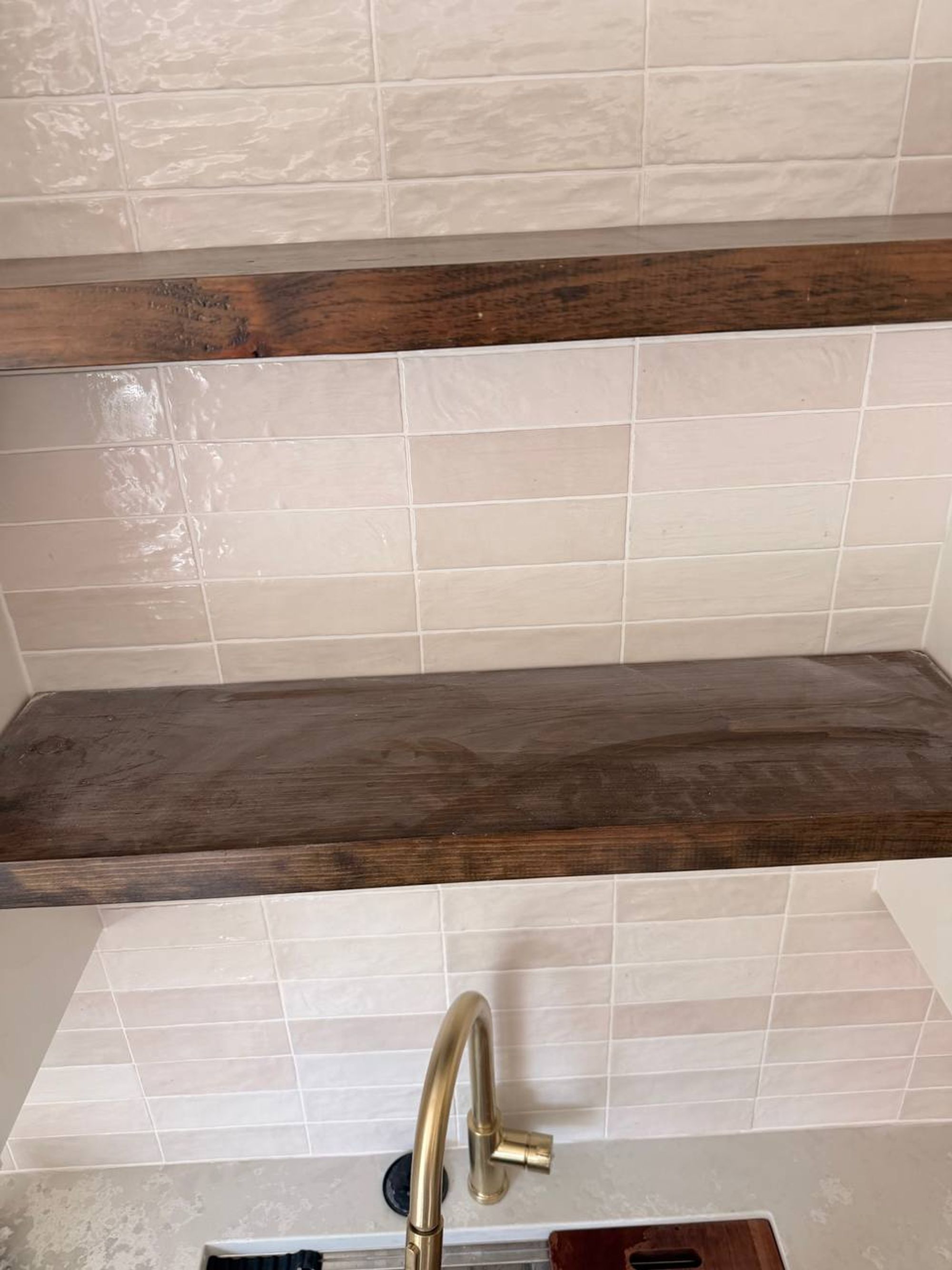 Dark wood floating shelves over a cream tile wall and brass faucet