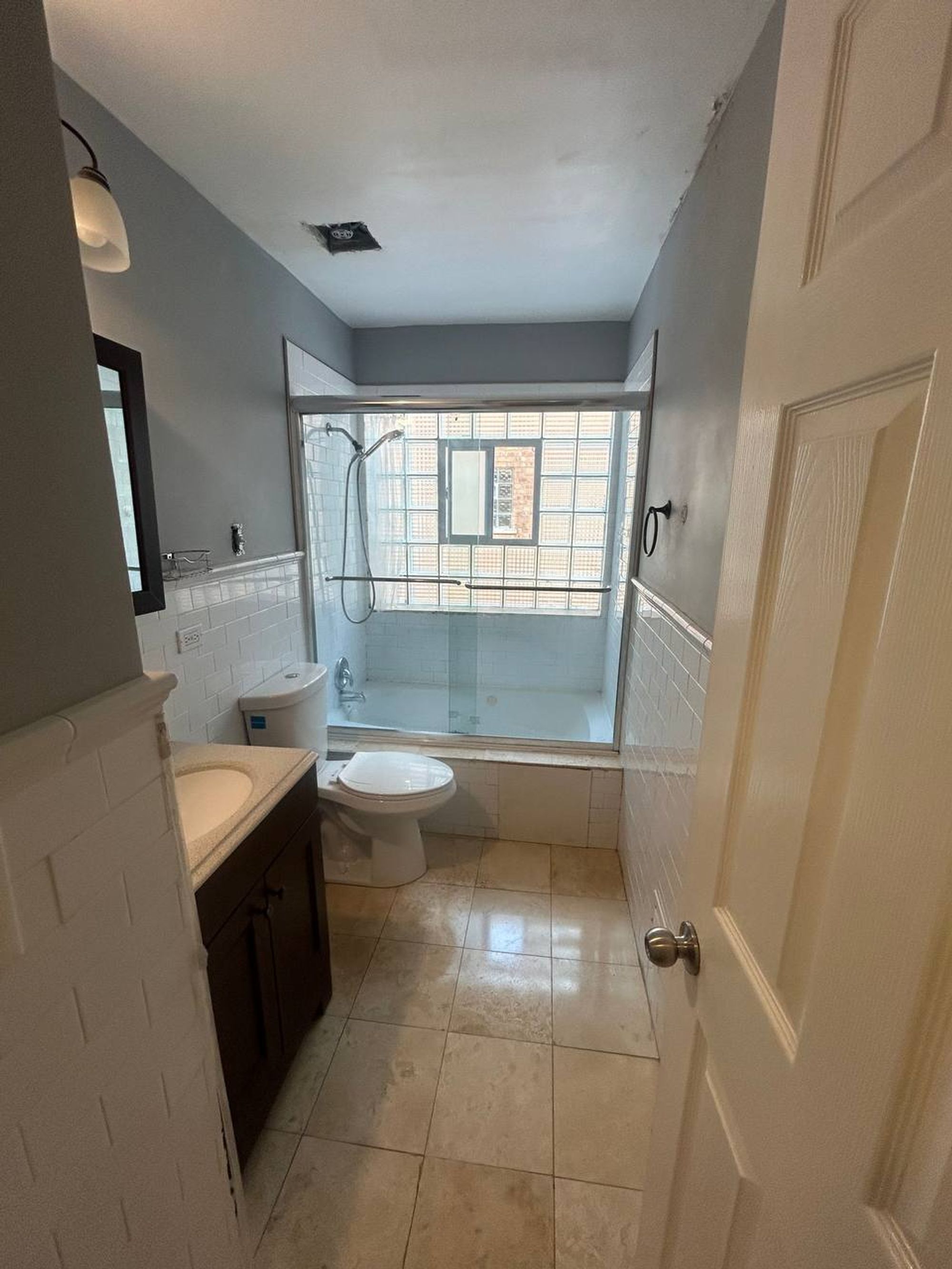 Bathroom with glass block window, tub, white tile and dark vanity