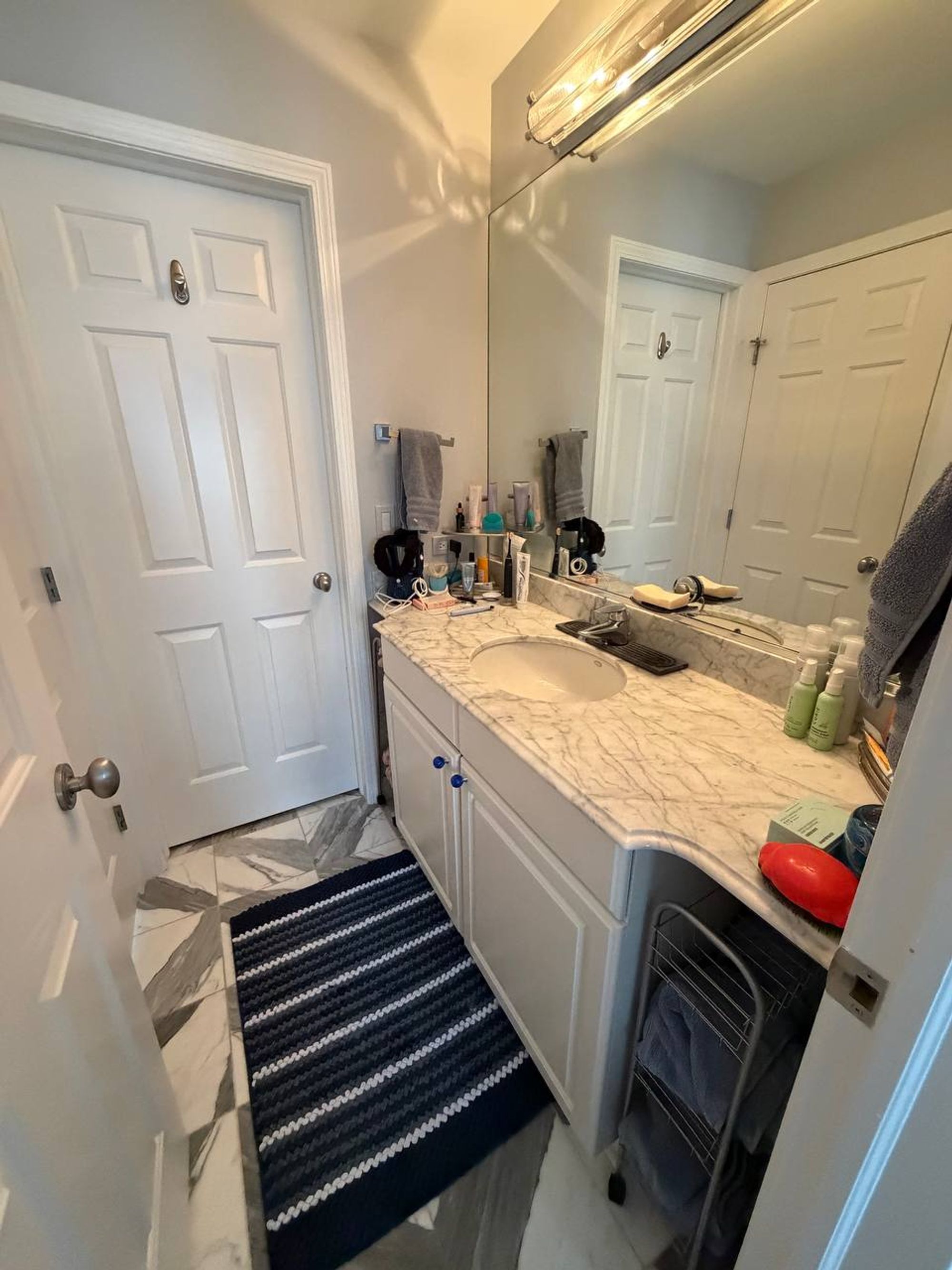 White vanity with marble counter, wide mirror and striped bath rug