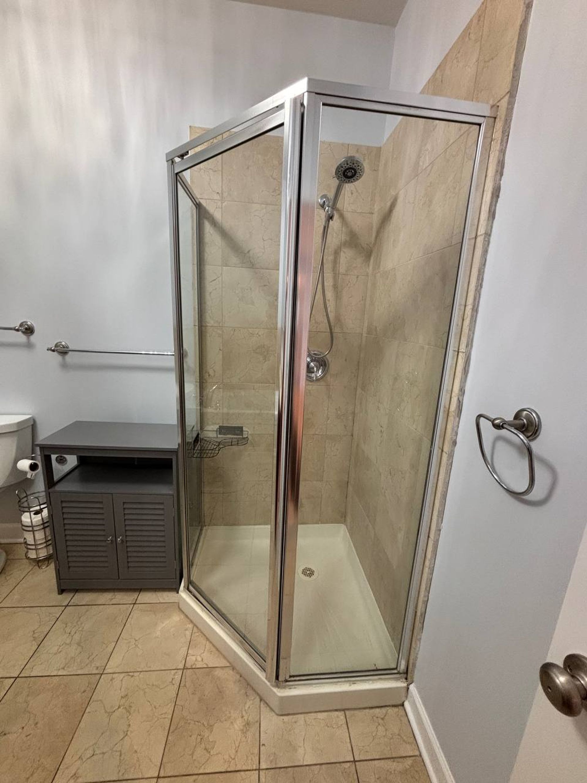 Corner shower with clear glass door and beige marble tile