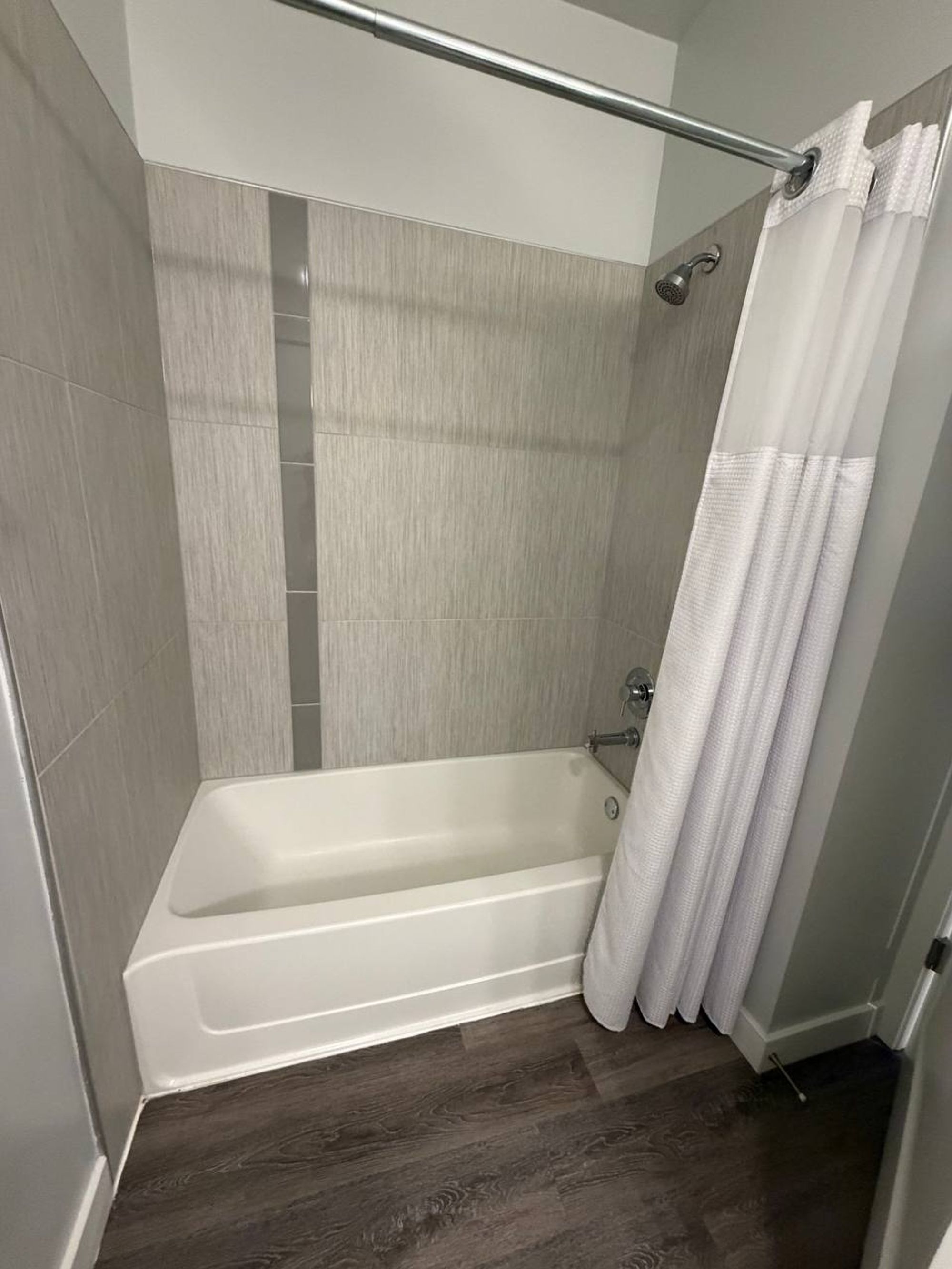 Tub with gray tile surround and white shower curtain