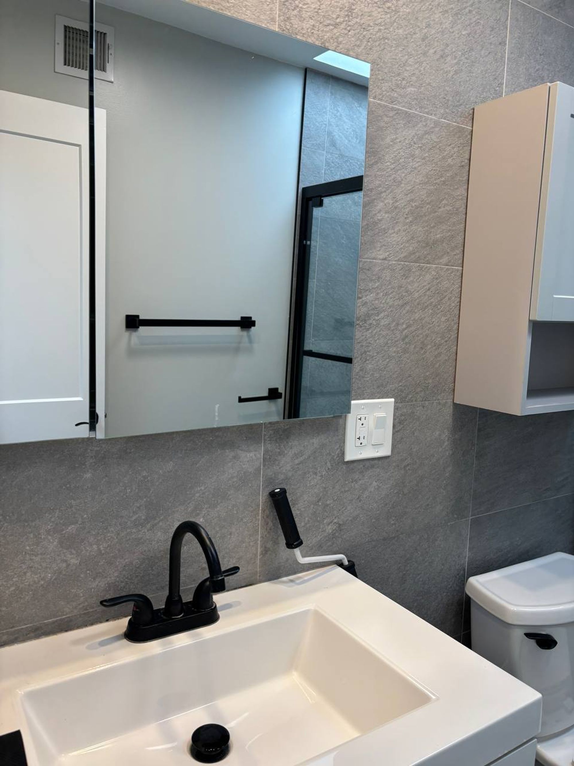 Clean white bathroom sink with black faucet and gray tile wall