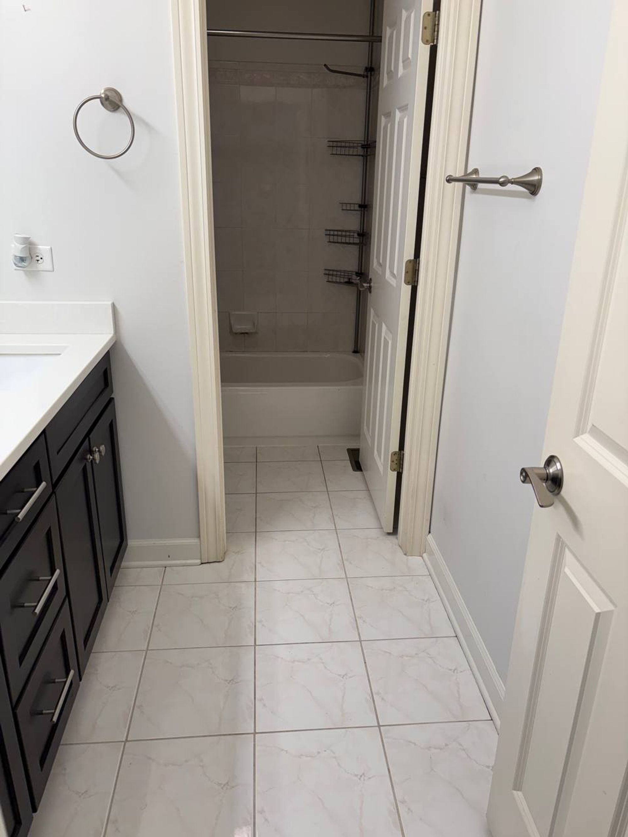 Bathroom floor tile leading past a dark vanity to a white tub