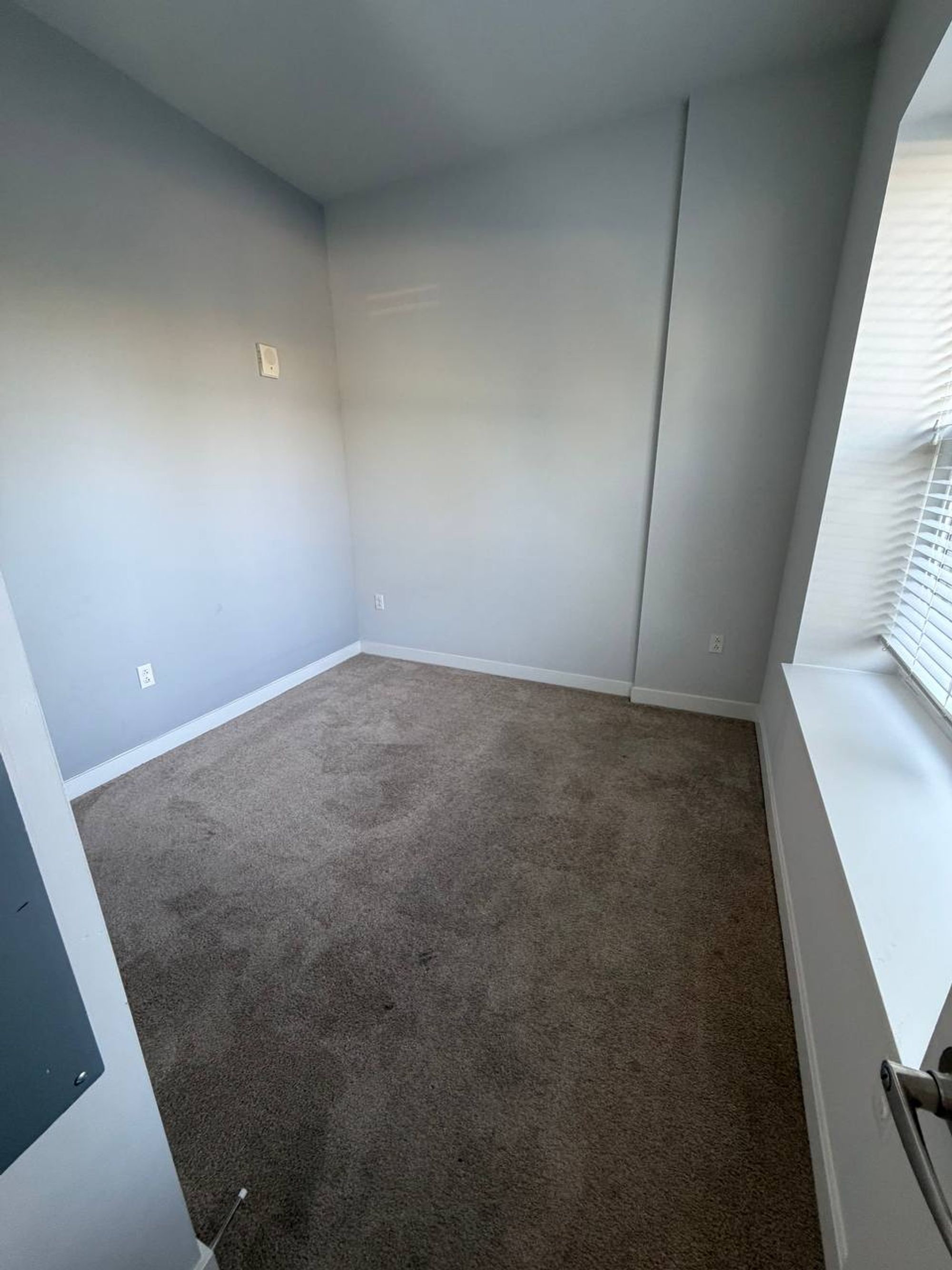 Small empty bedroom with vacuumed carpet and window blinds