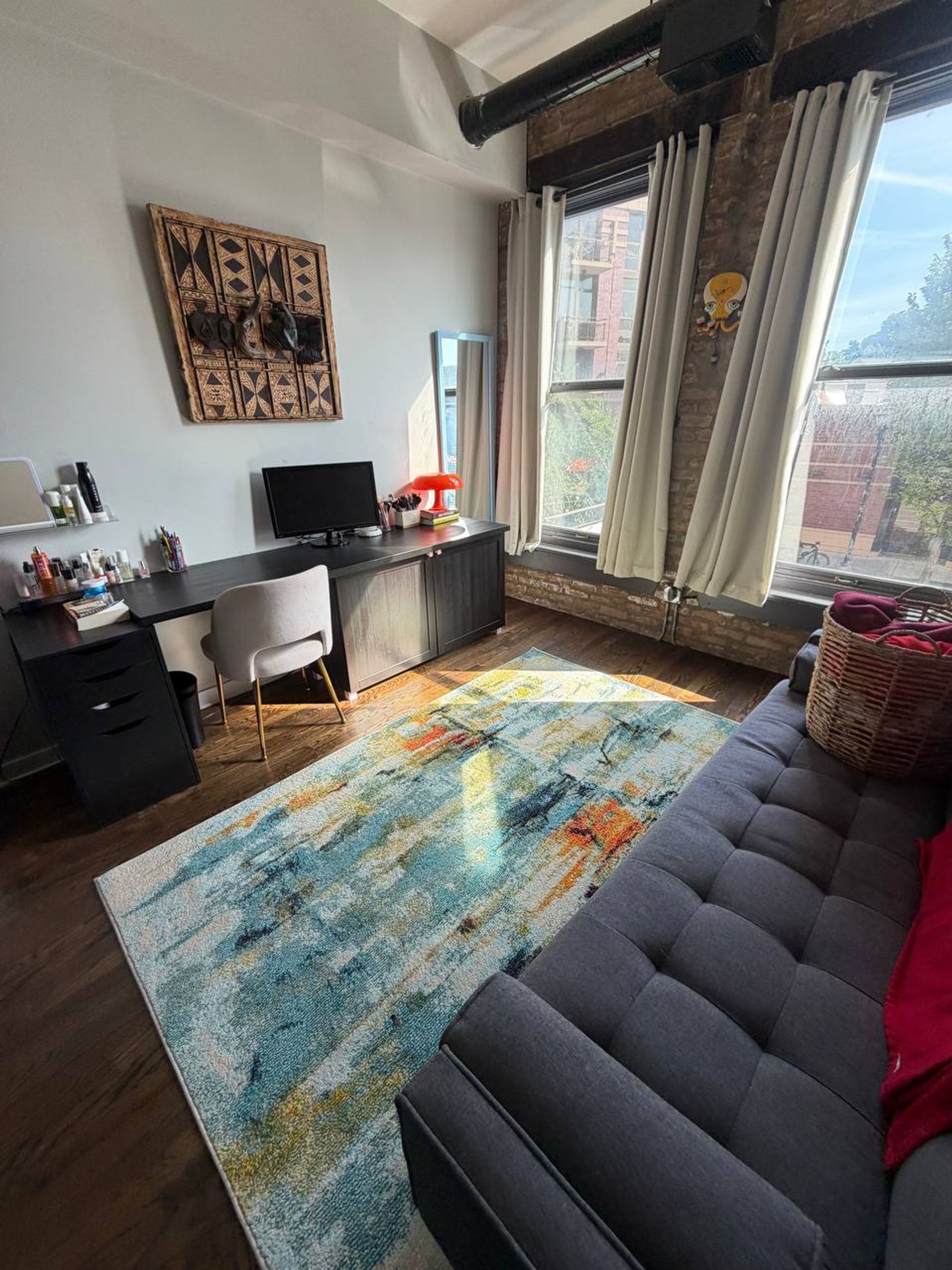 Loft living room with exposed brick, desk, gray sofa and colorful rug