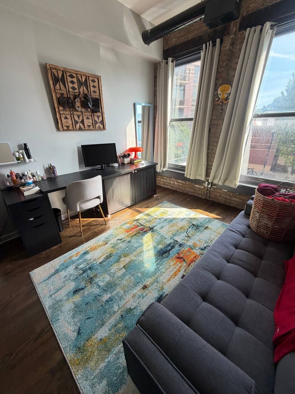 Loft living room with exposed brick, desk, gray sofa and colorful rug