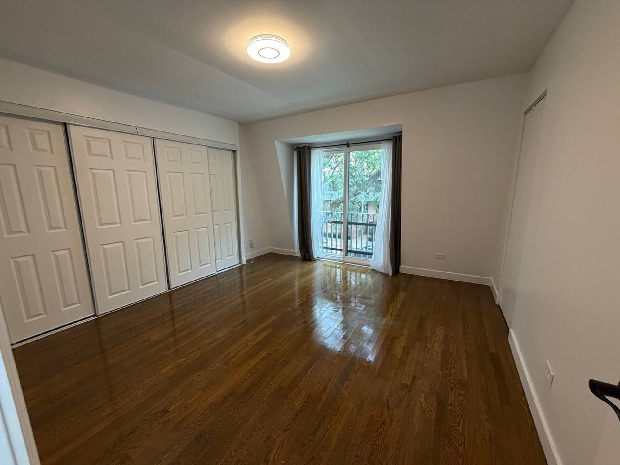 Empty bedroom with white sliding closet doors and polished wood floor