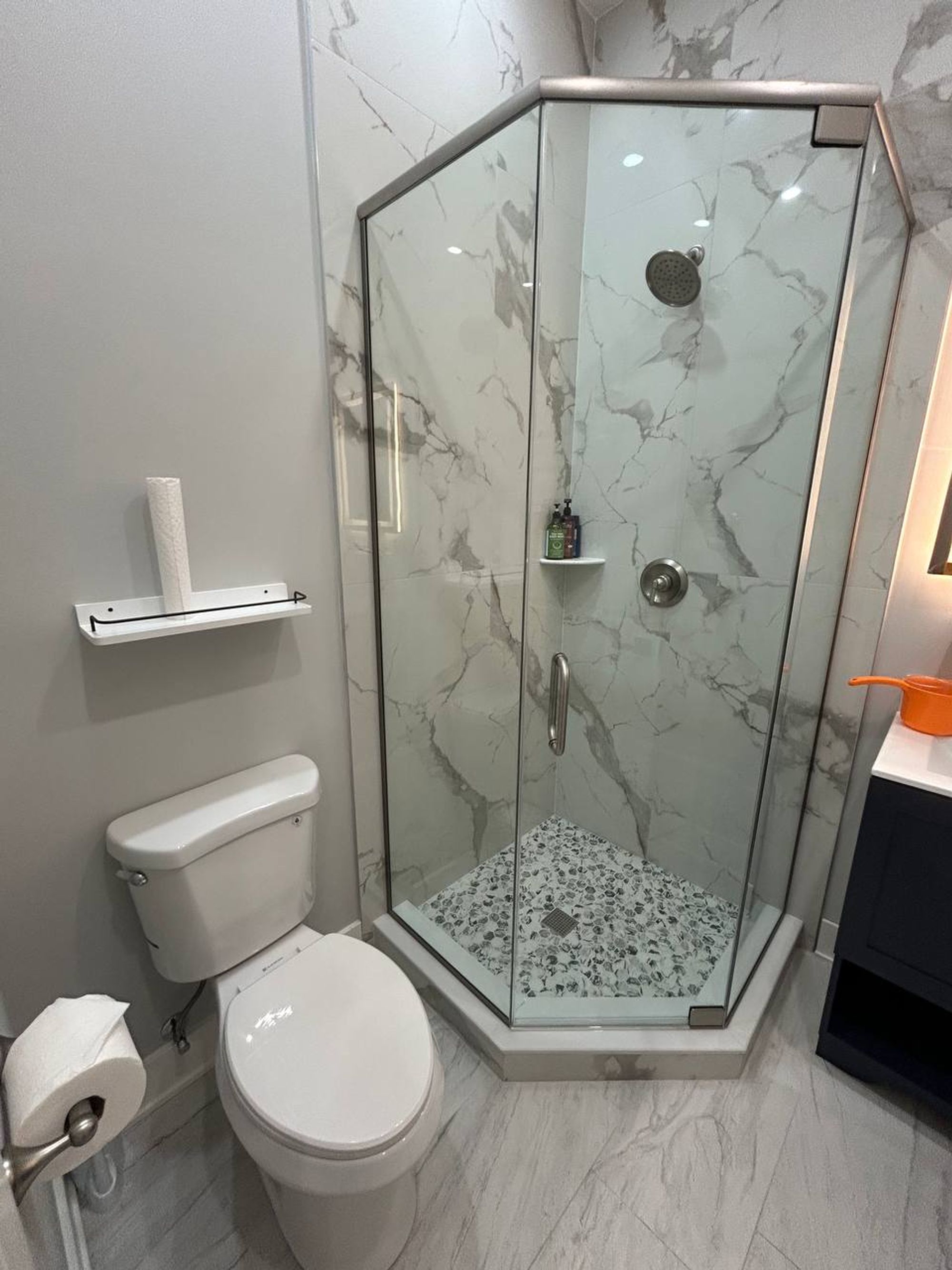 Glass corner shower with marble look tile beside white toilet