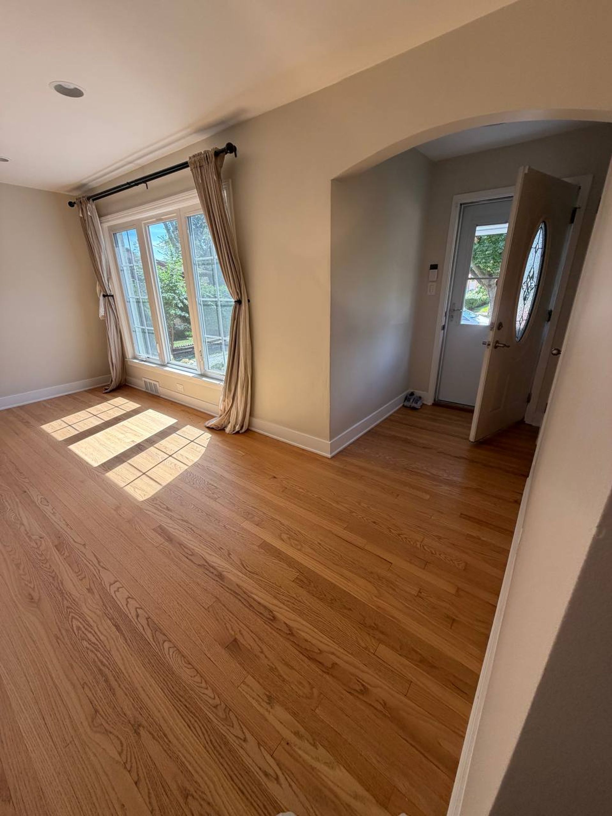Empty living room with oak floors, curtained windows and arched entry