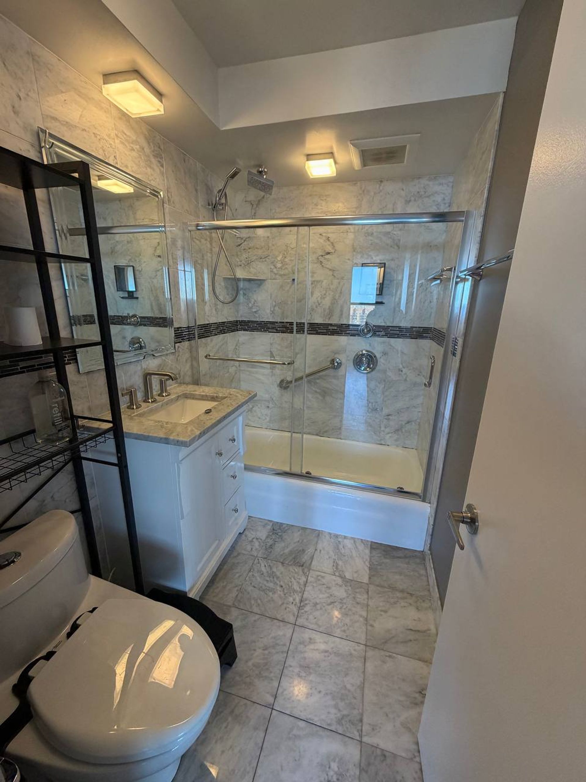 Marble tiled bathroom with white vanity and sliding glass tub doors