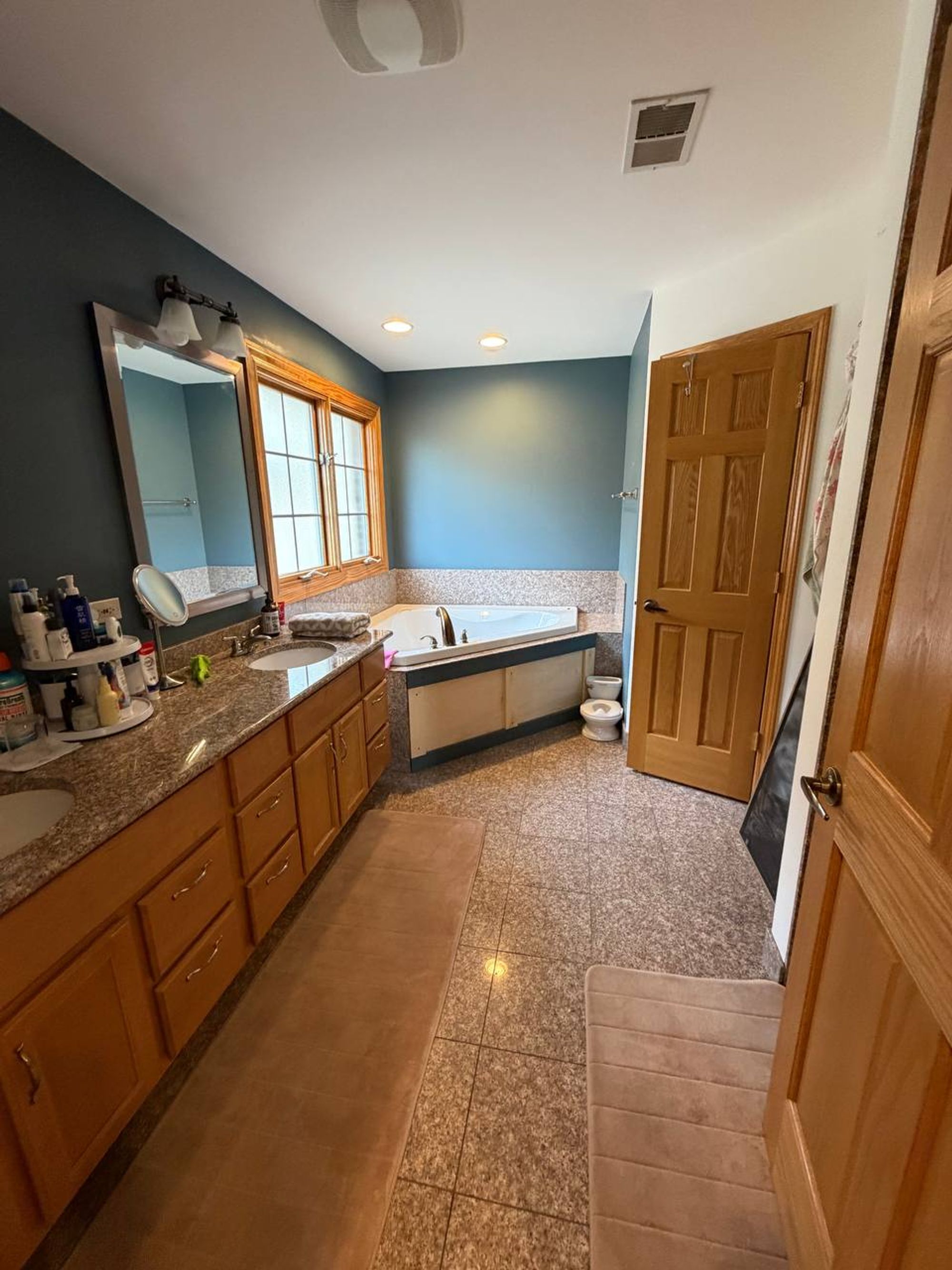 Primary bathroom with long double vanity, corner tub and tile floor