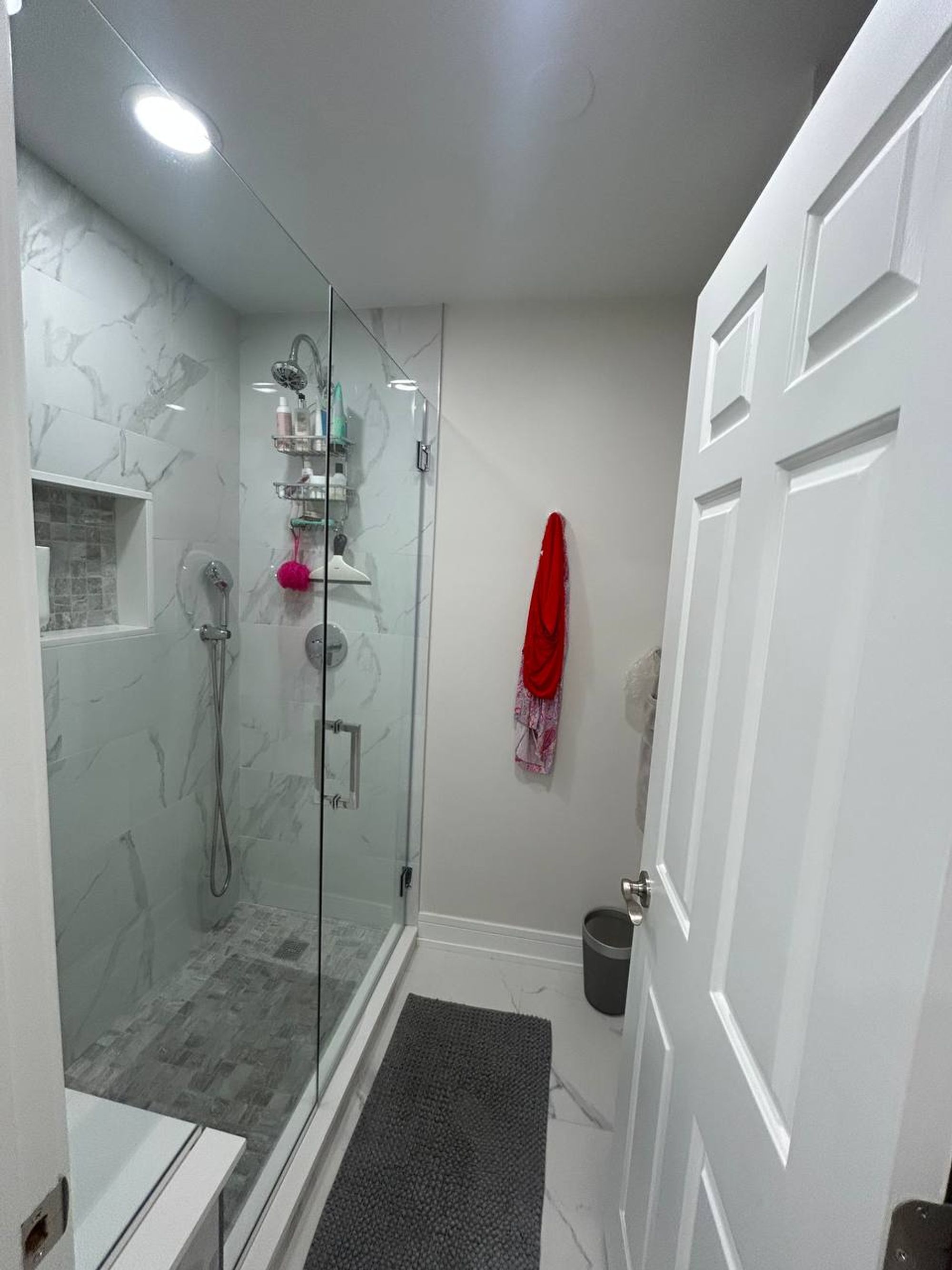 Bathroom with glass walk-in shower, marble look tile and gray bath mat
