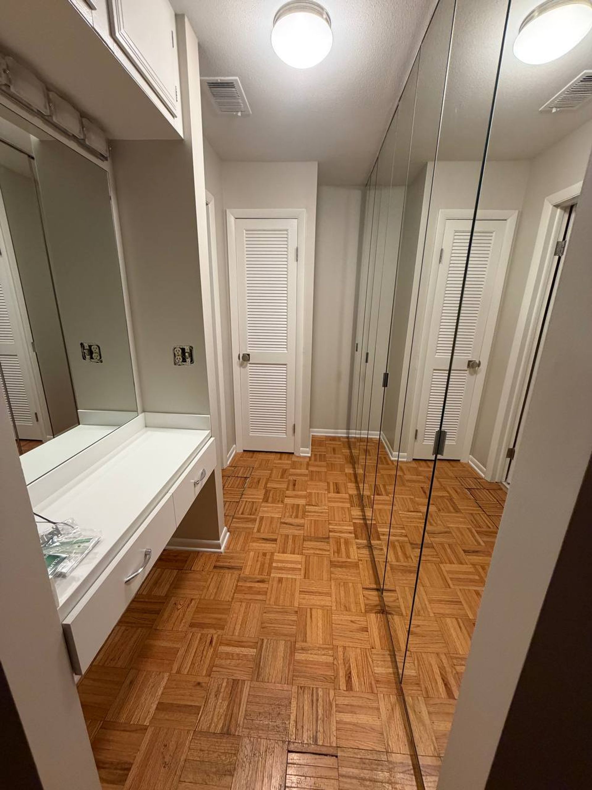 Dressing hallway with mirrored closet doors, white vanity and parquet floor