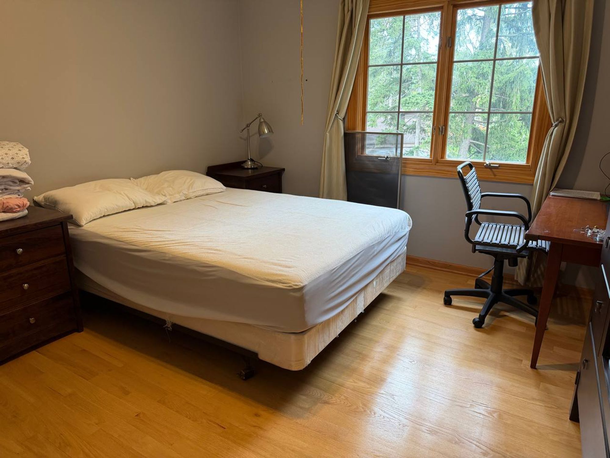 Guest bedroom with made bed, desk chair and hardwood floor