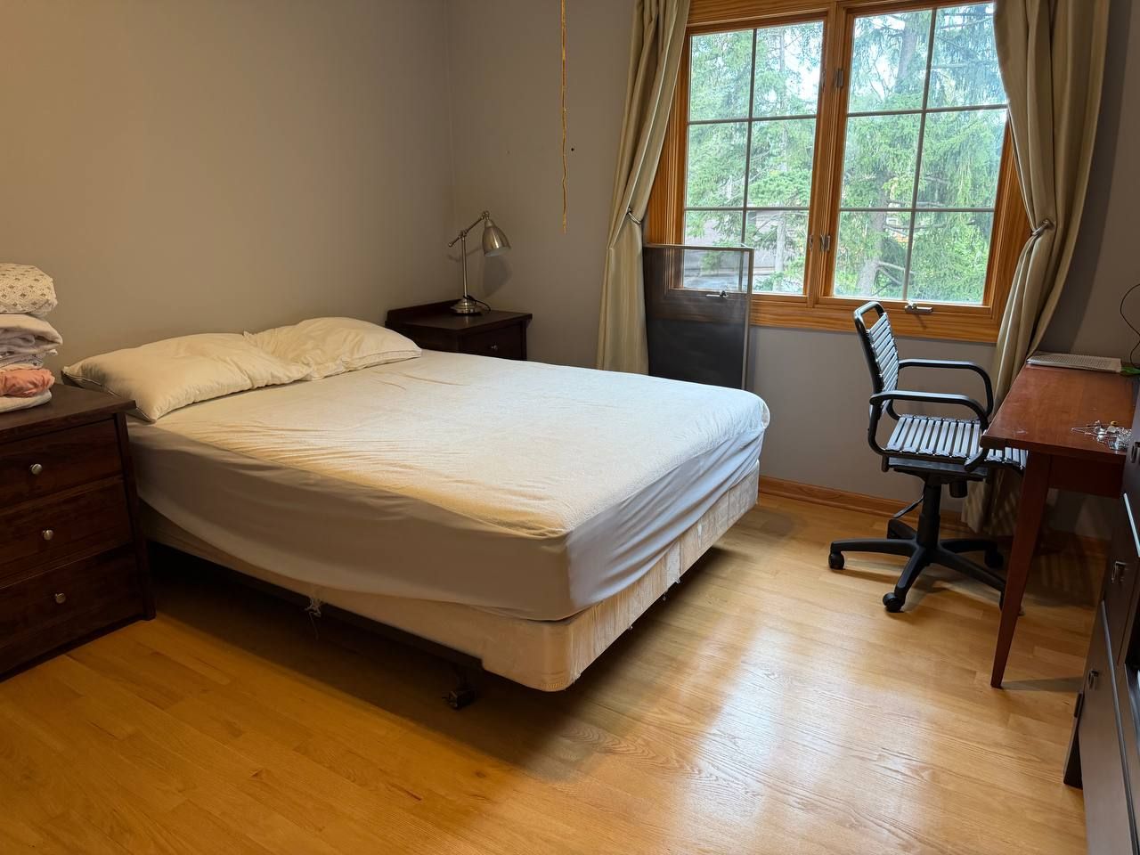 Guest bedroom with made bed, desk chair and hardwood floor