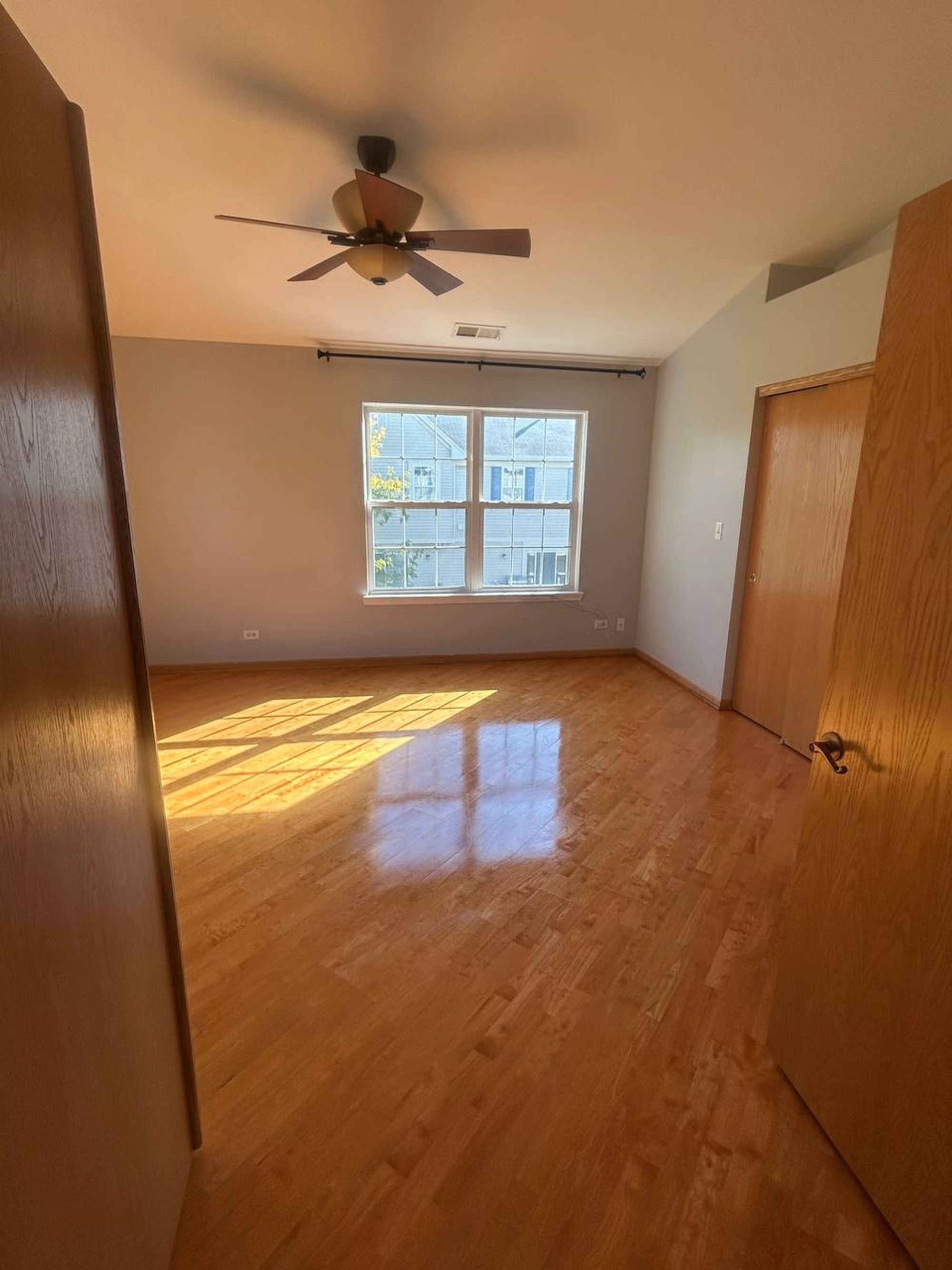 Empty bedroom with ceiling fan and shiny hardwood floor