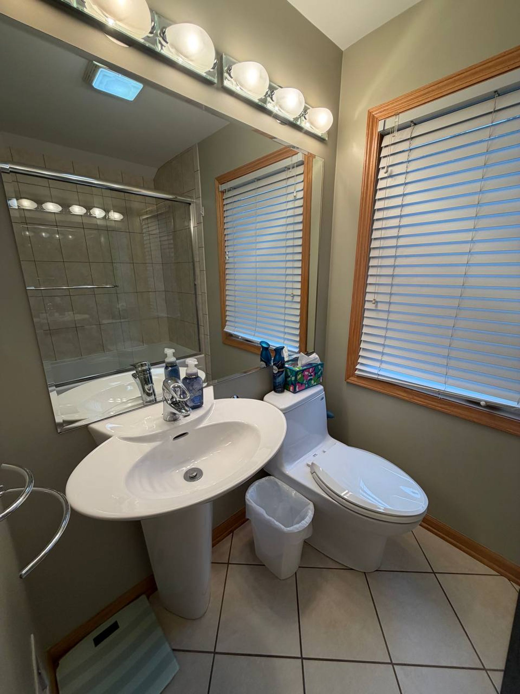 Bathroom with pedestal sink, wide mirror and two windows with blinds