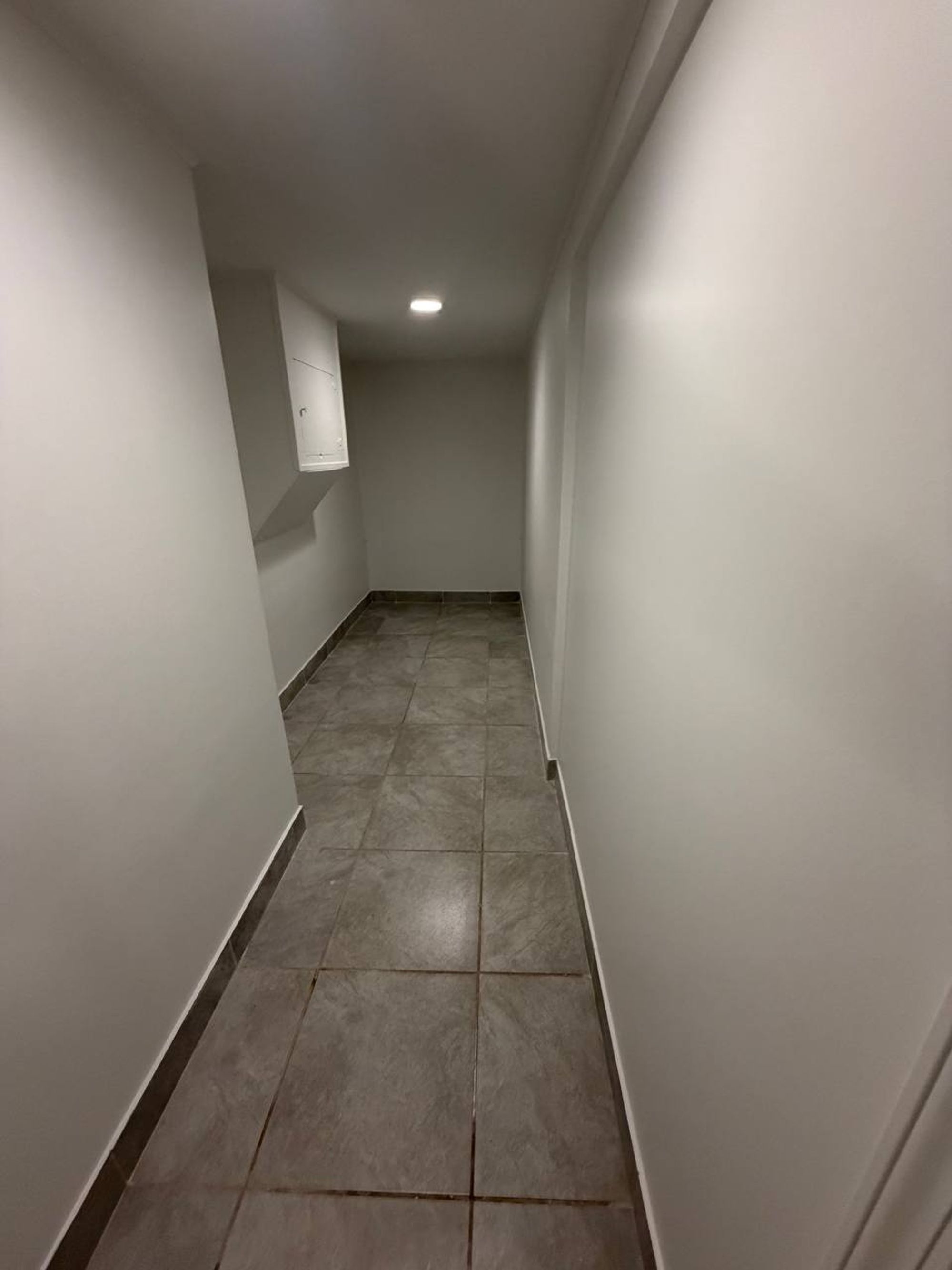 Narrow basement hallway with gray tile floor and white walls