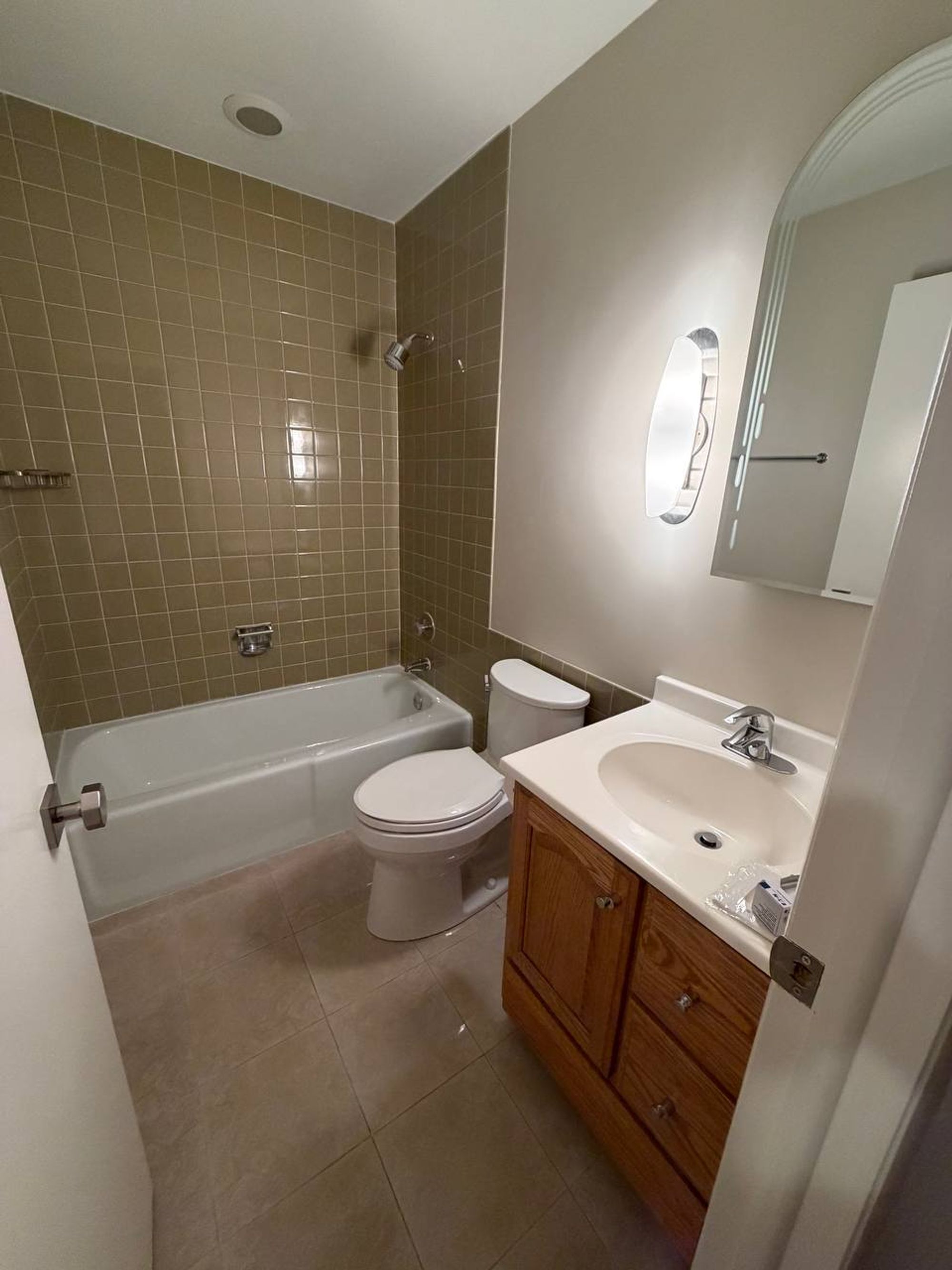 Bathroom with green tiled tub, white toilet and oak vanity