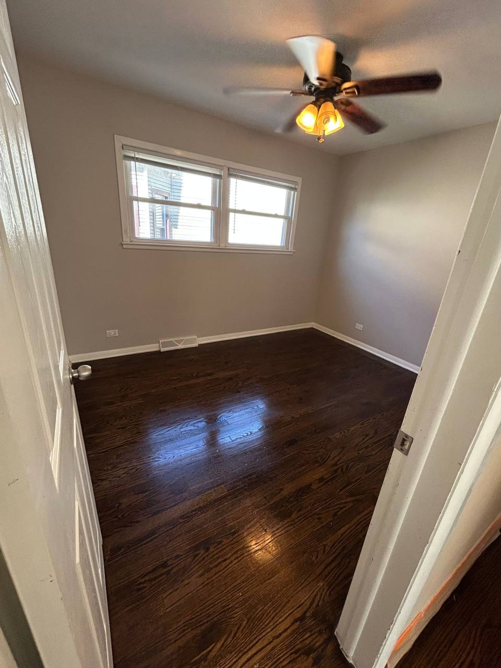 Empty bedroom with ceiling fan and shiny dark hardwood floor