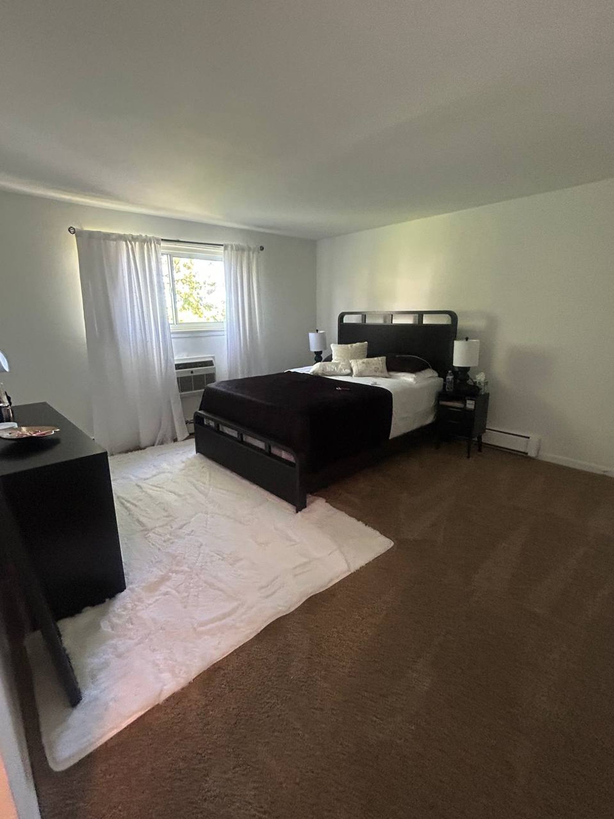 Bedroom with dark wood bed, white rug and vacuumed brown carpet