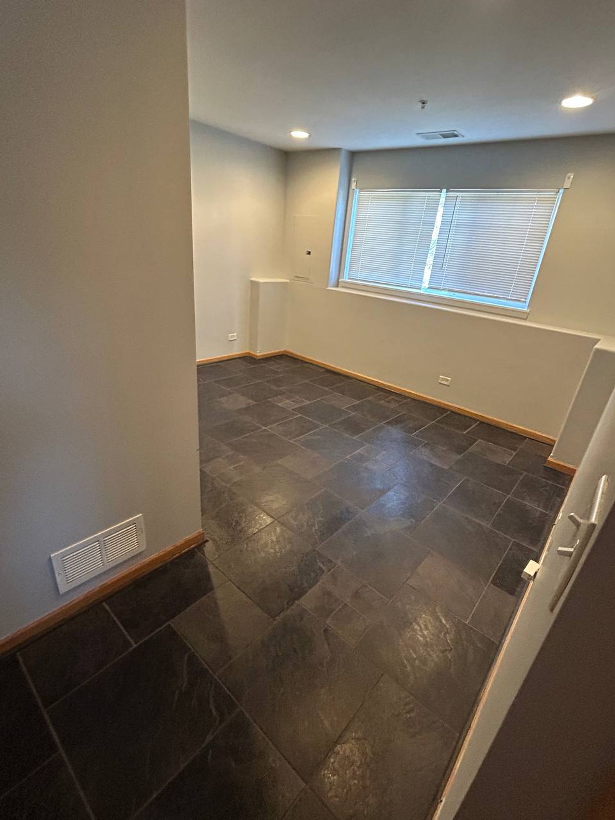 Empty lower-level room with slate tile floor and window blinds