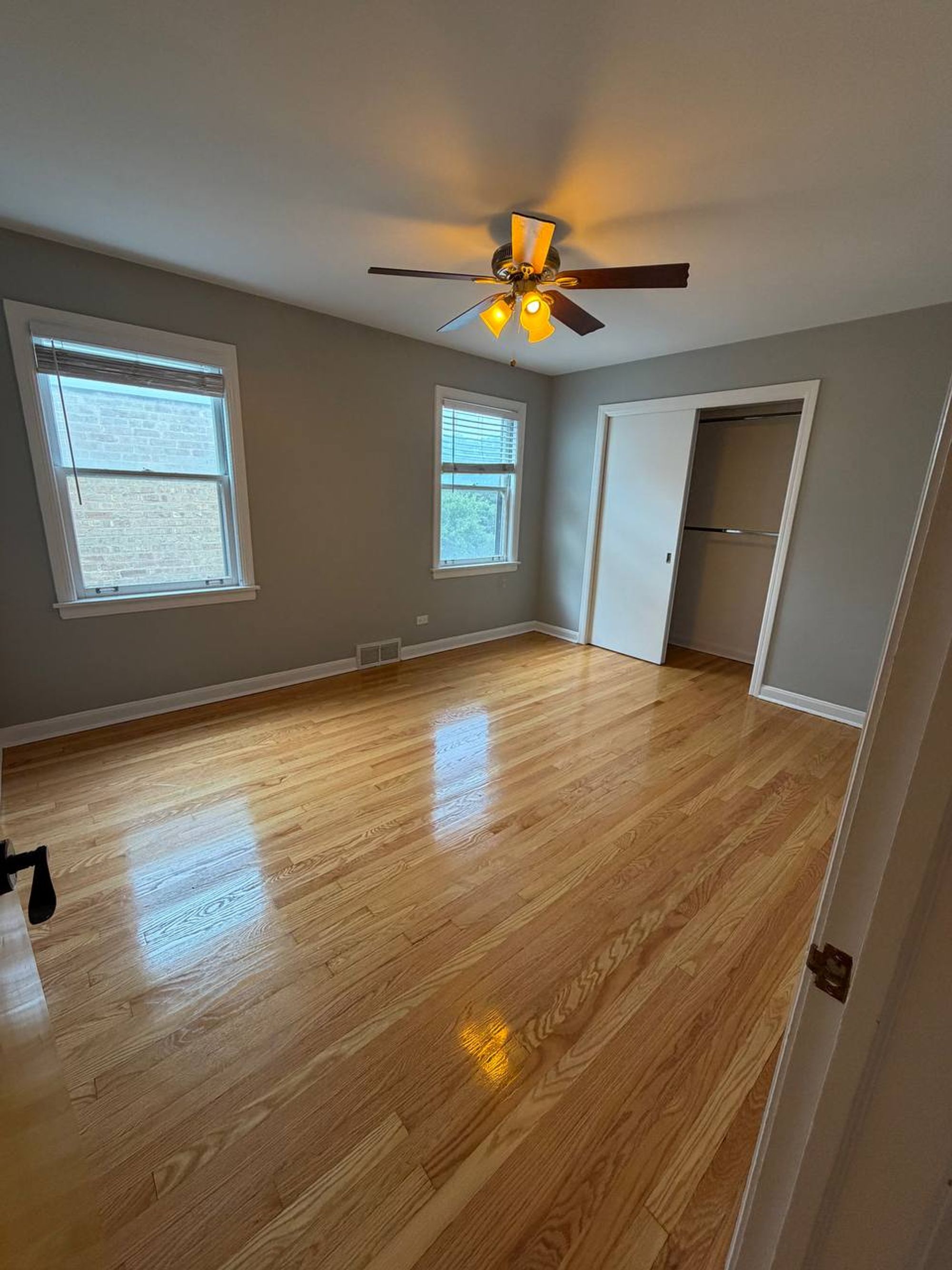 Empty bedroom with ceiling fan, open closet and glossy oak floor