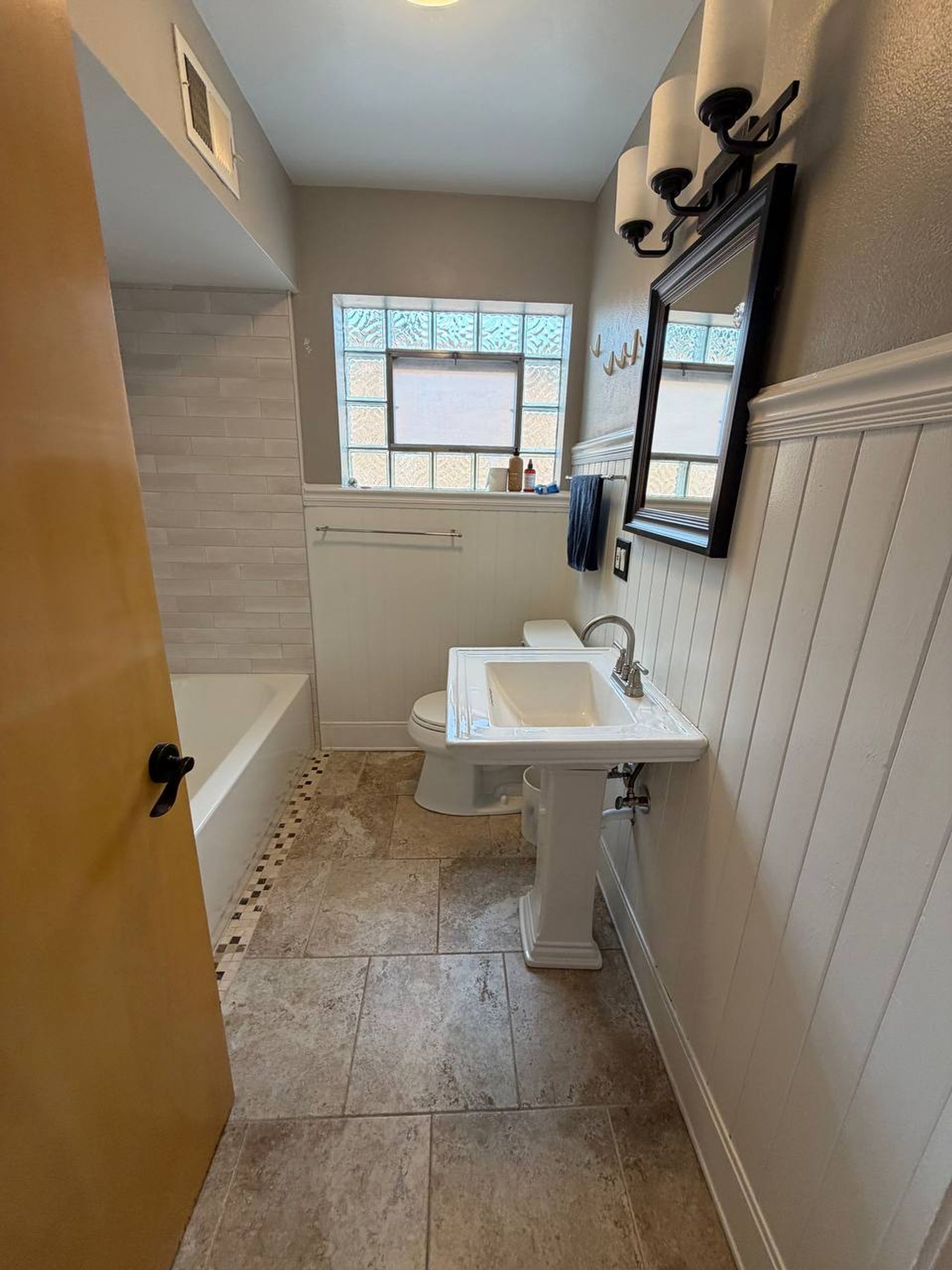 Bathroom with white tub, pedestal sink and white wood paneling