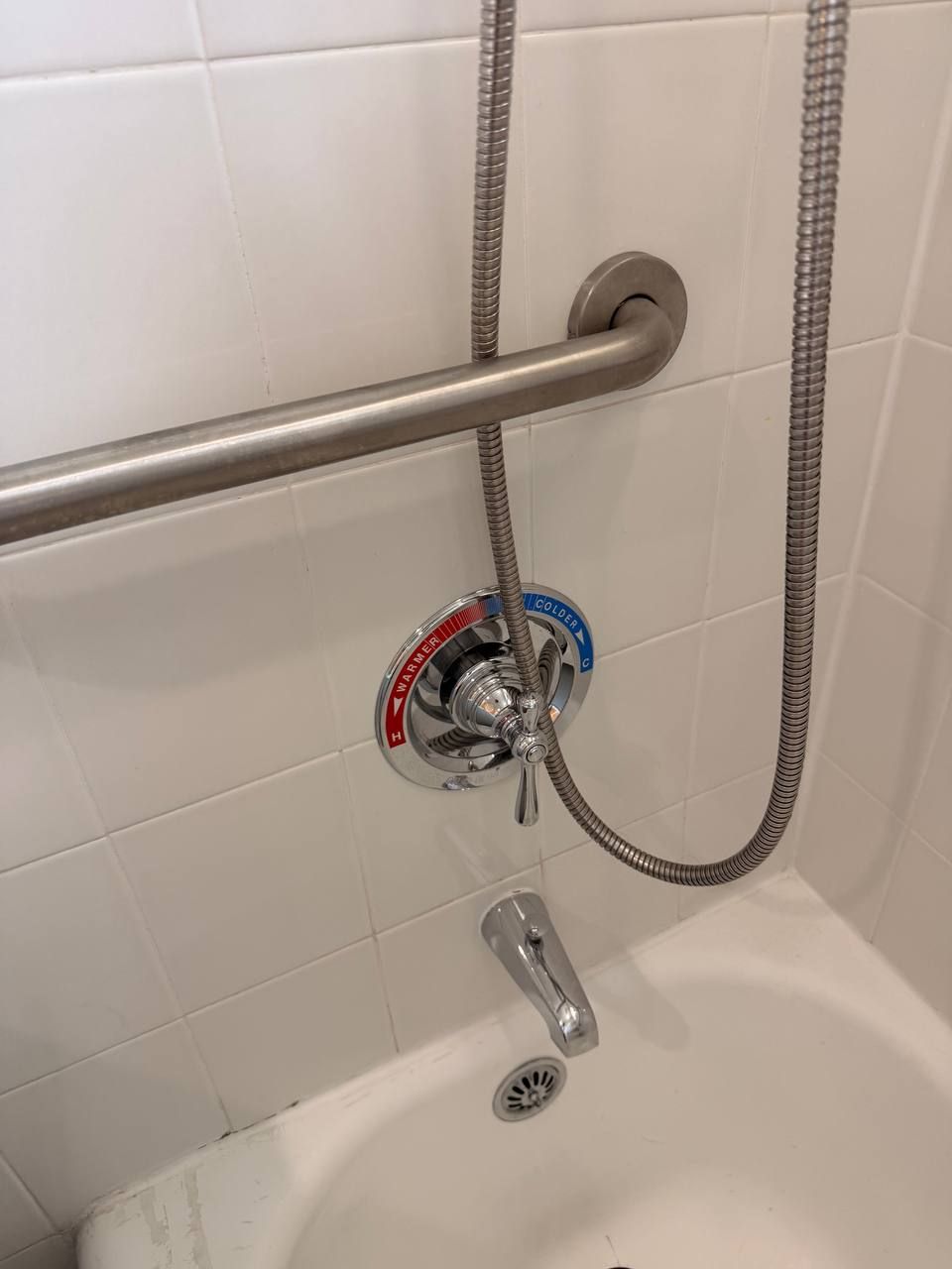 White tile tub wall with grab bar, dial and handheld shower