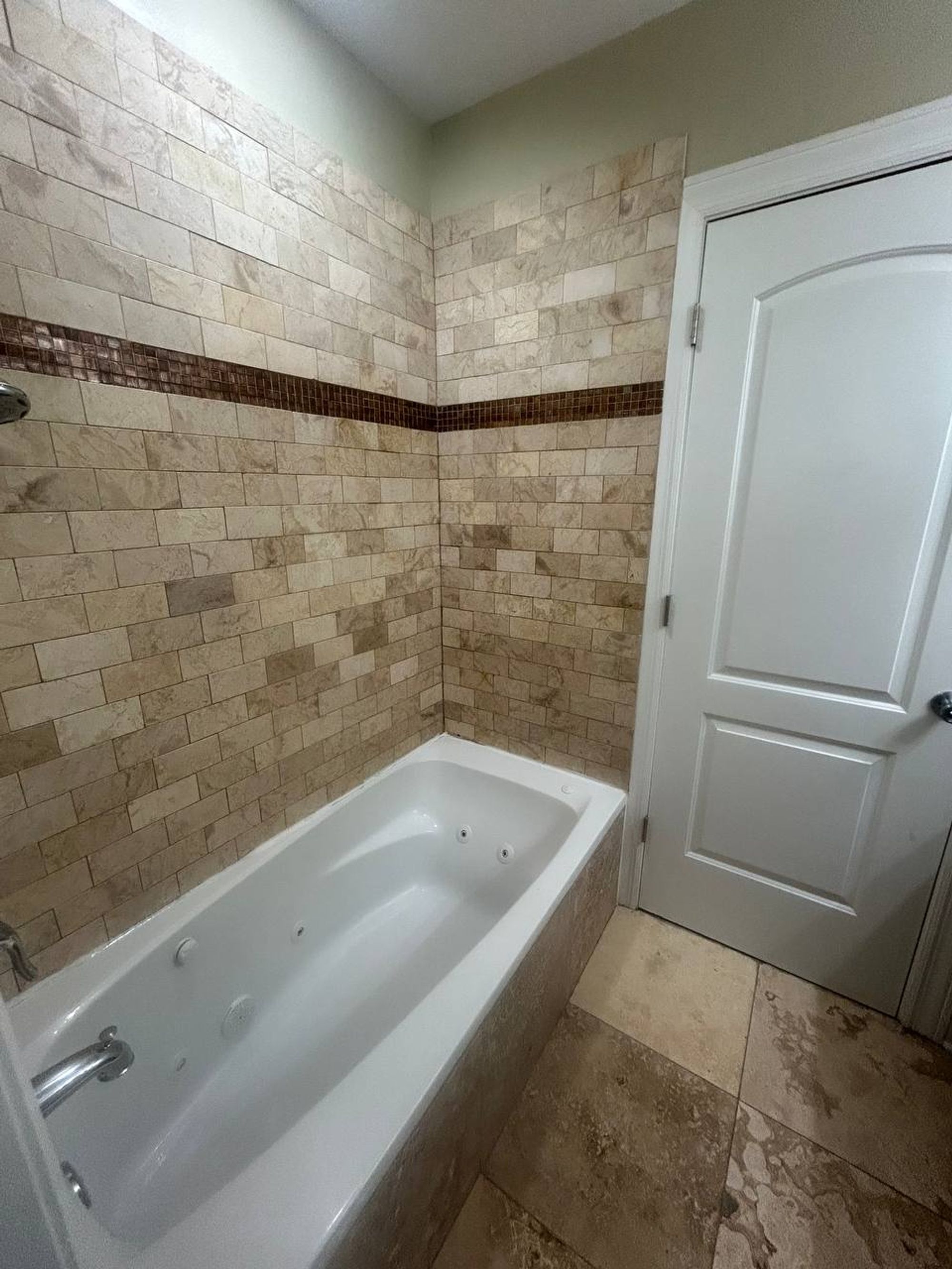 White jetted tub with travertine tile and glass mosaic band