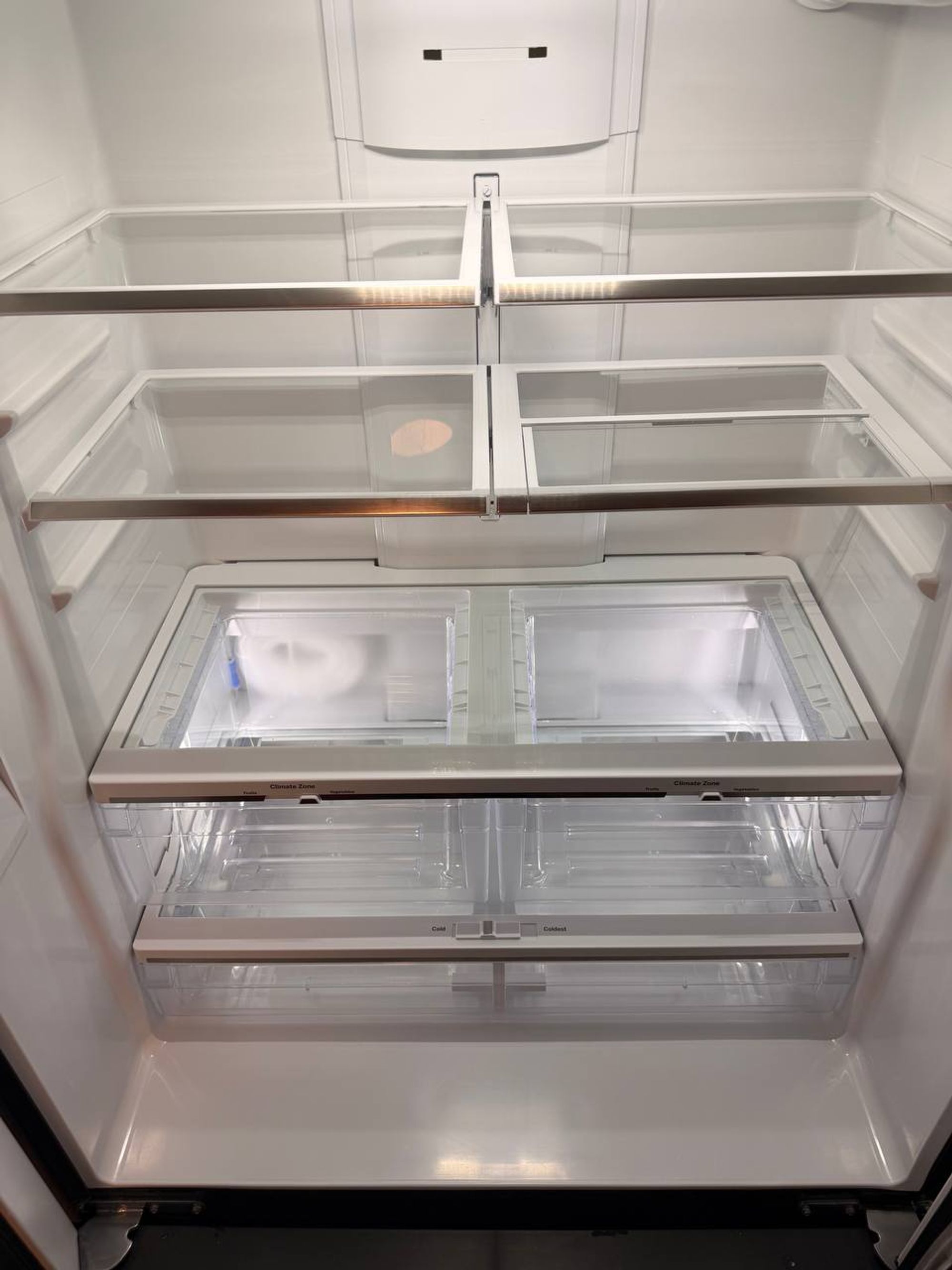 Empty refrigerator with clear glass shelves and clean crisper drawers