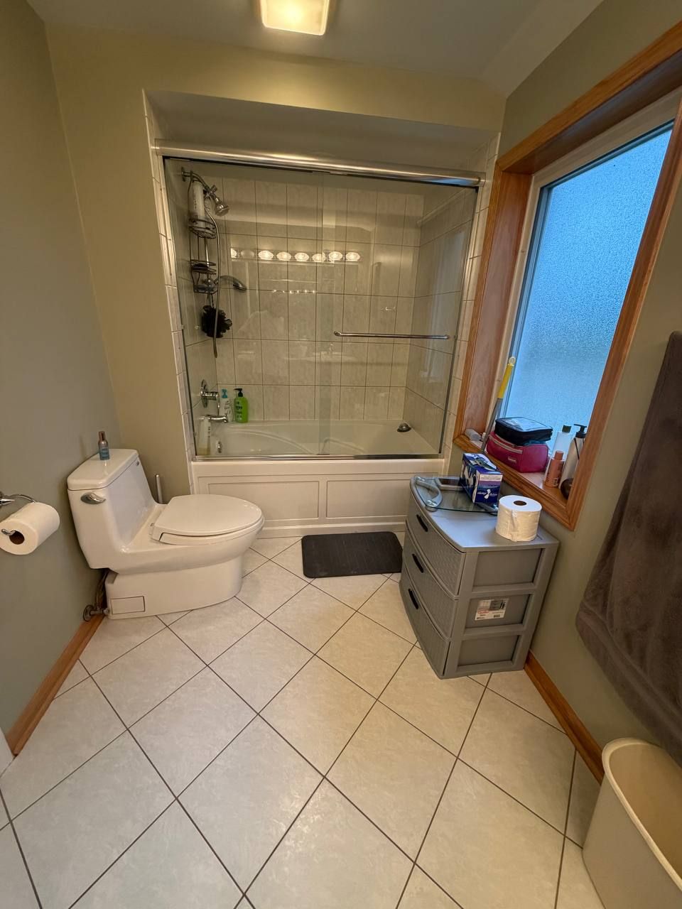 Bathroom with glass tub doors, toilet and tidy white floor tiles