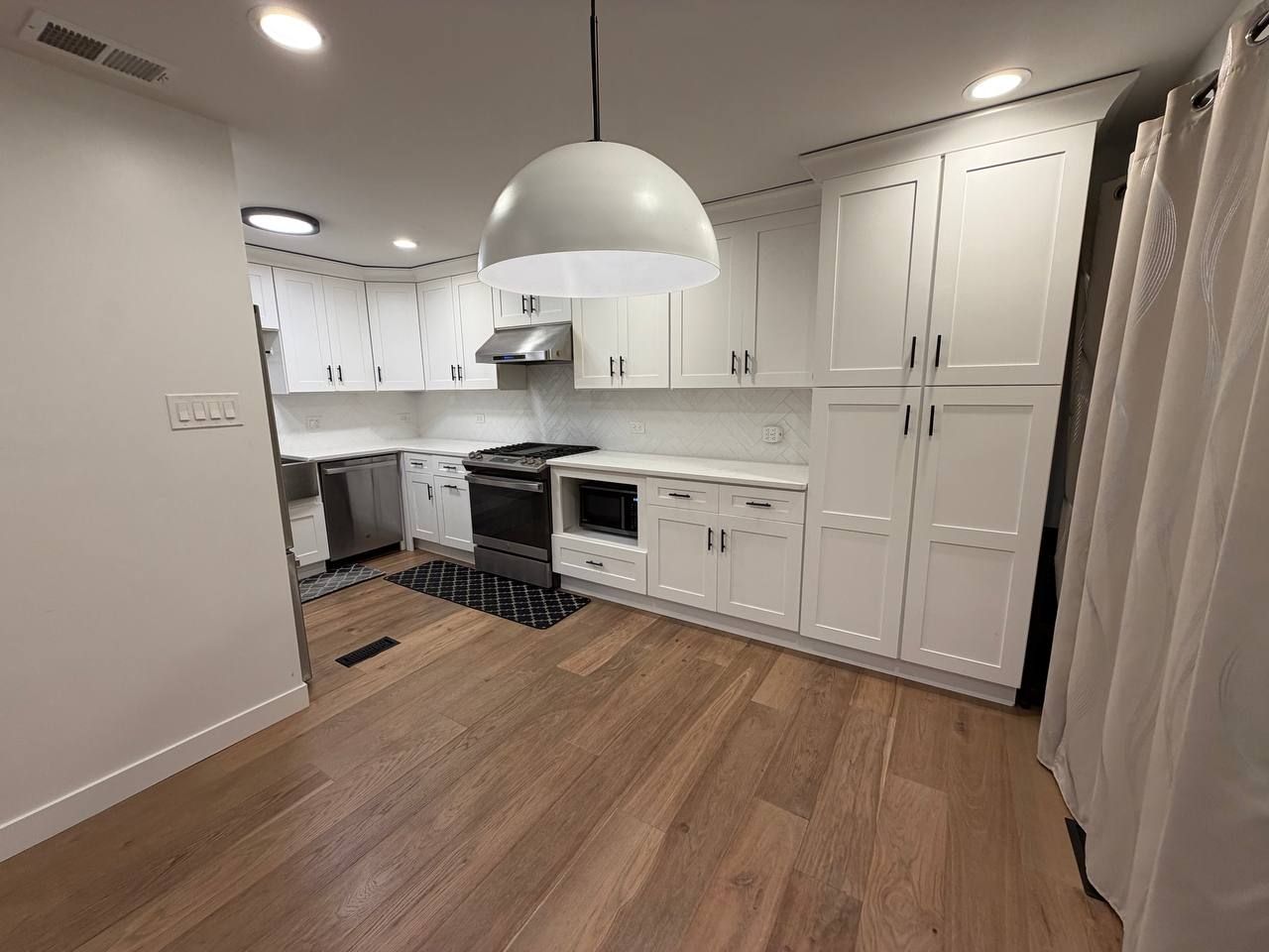Clean white shaker kitchen with pendant light and wood plank floor