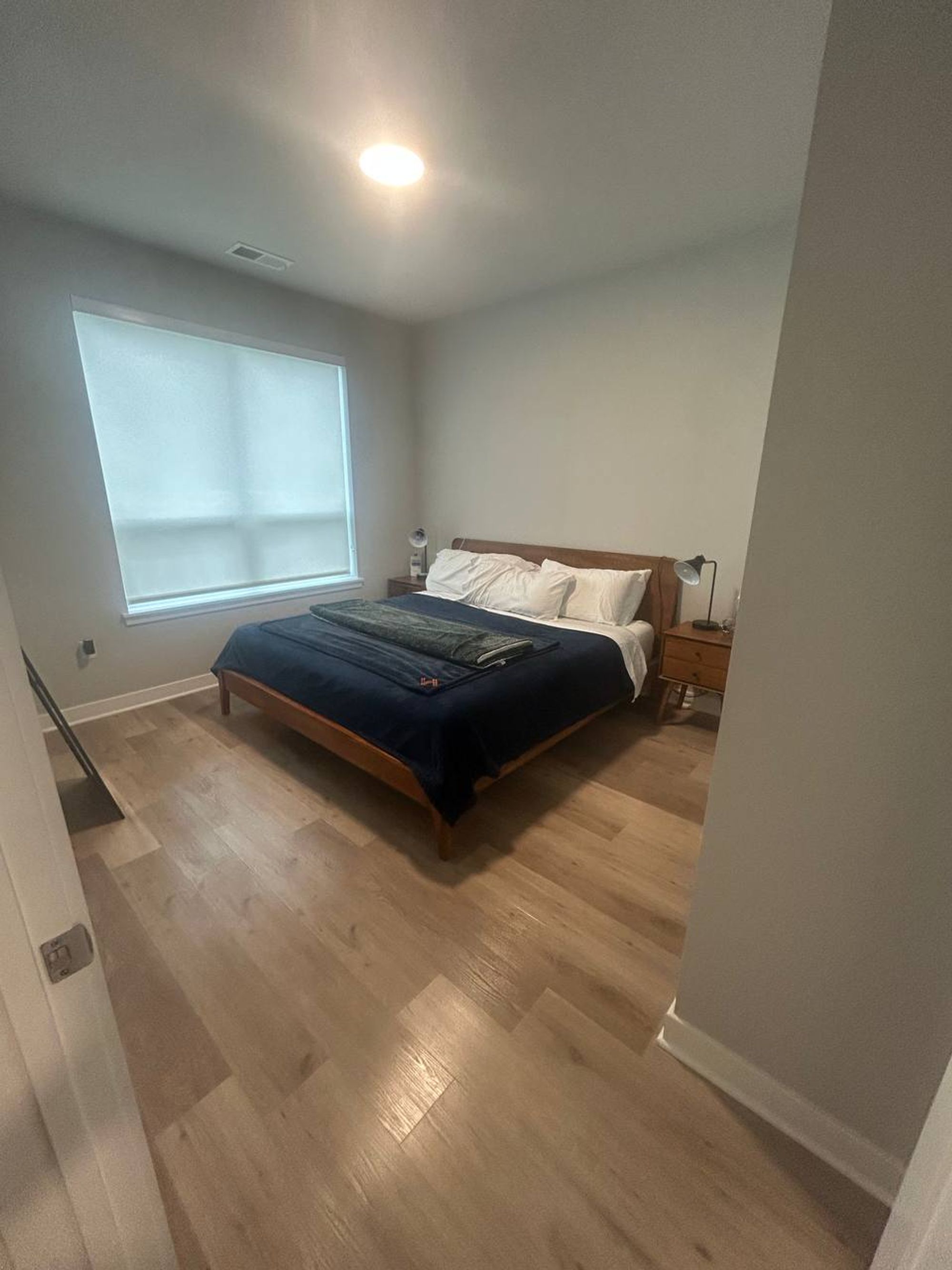 Bedroom with wood bed frame, navy bedding and light plank floor