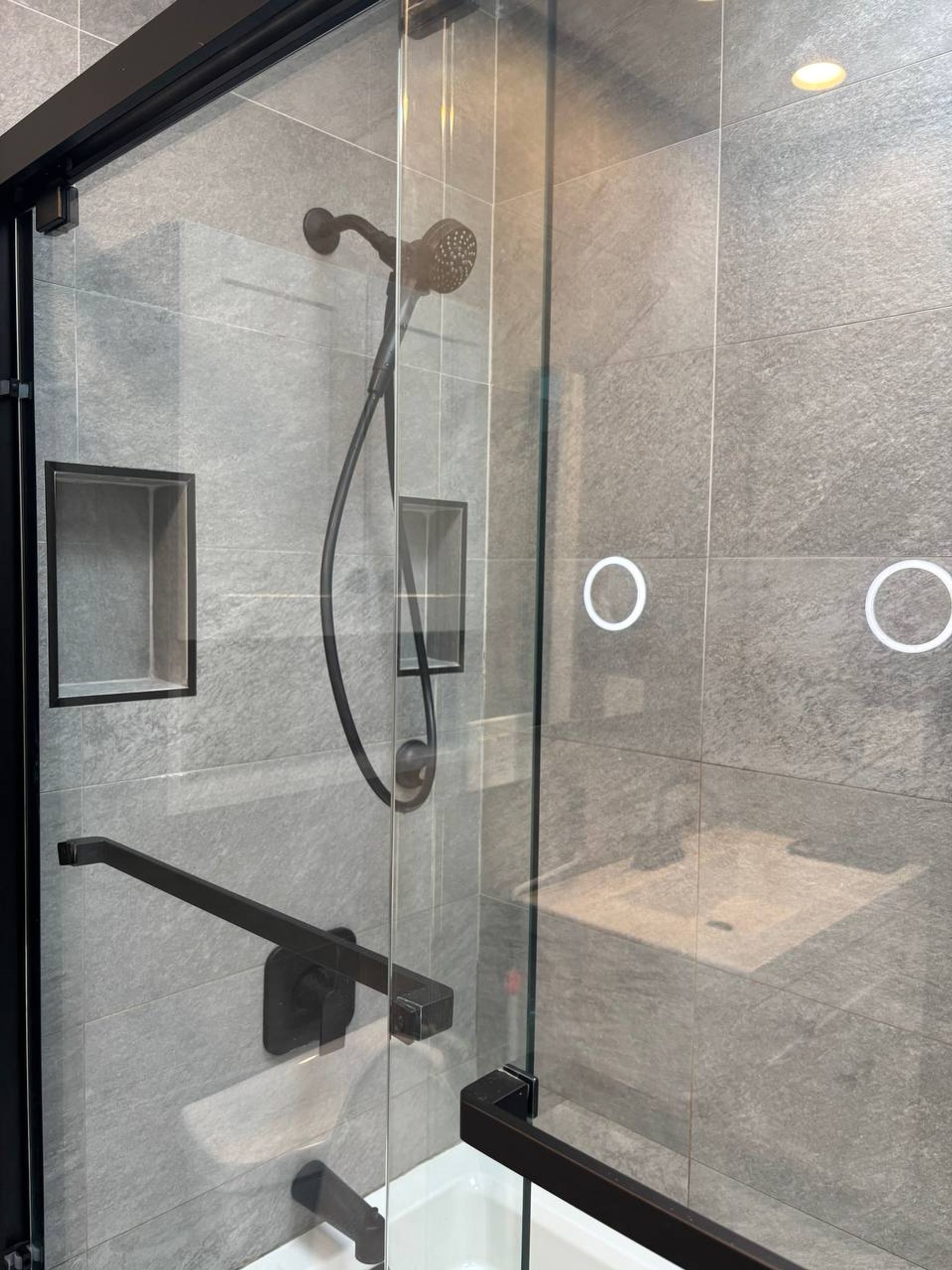 Glass tub door and gray tile shower with black fixtures