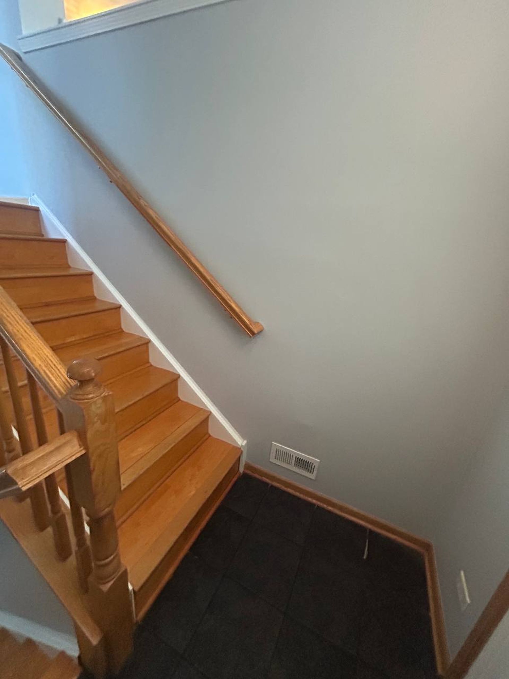 Wood staircase with oak railing leading down to a tile landing