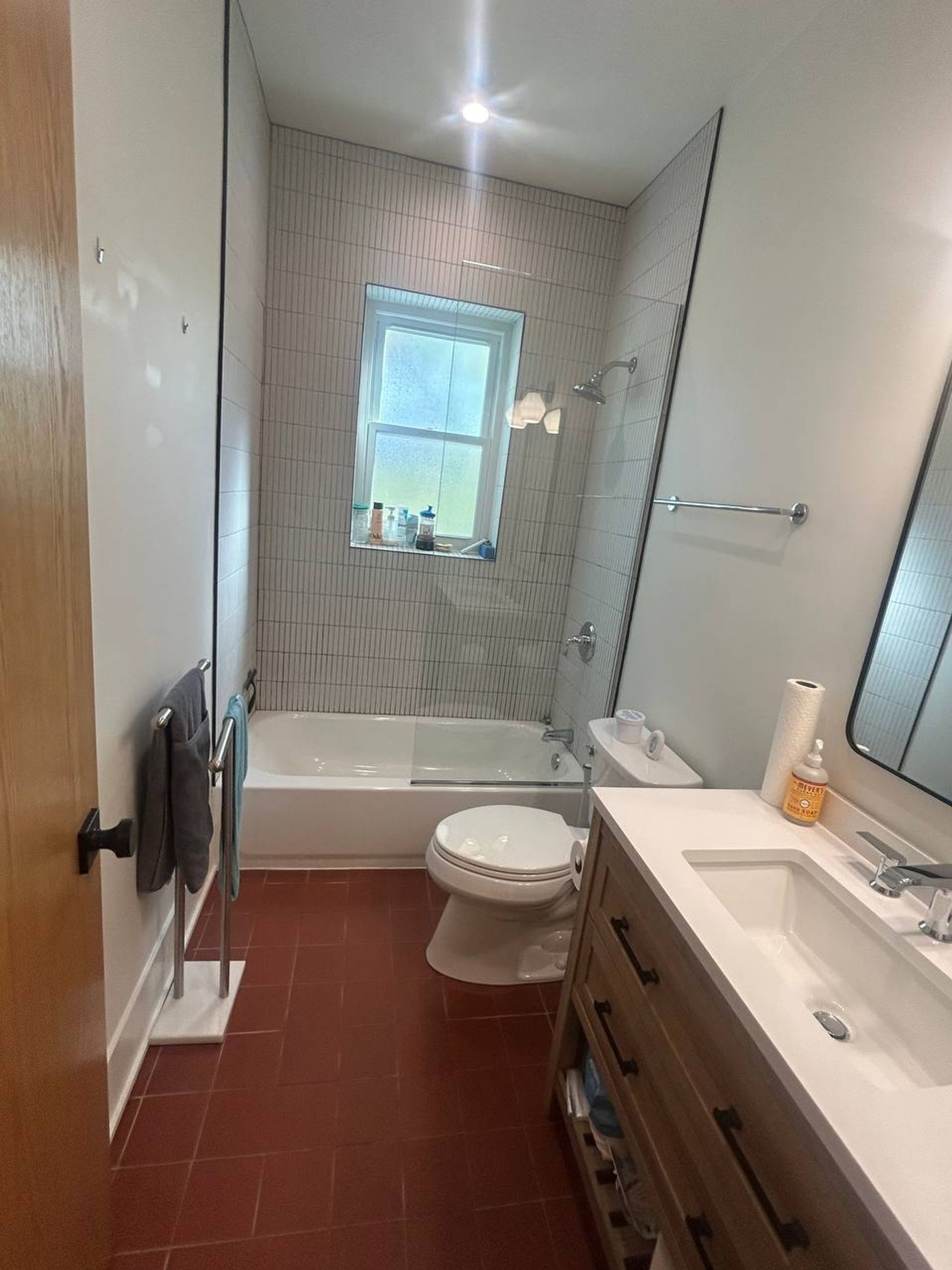 Bathroom with red tile floor, white tub and wood vanity