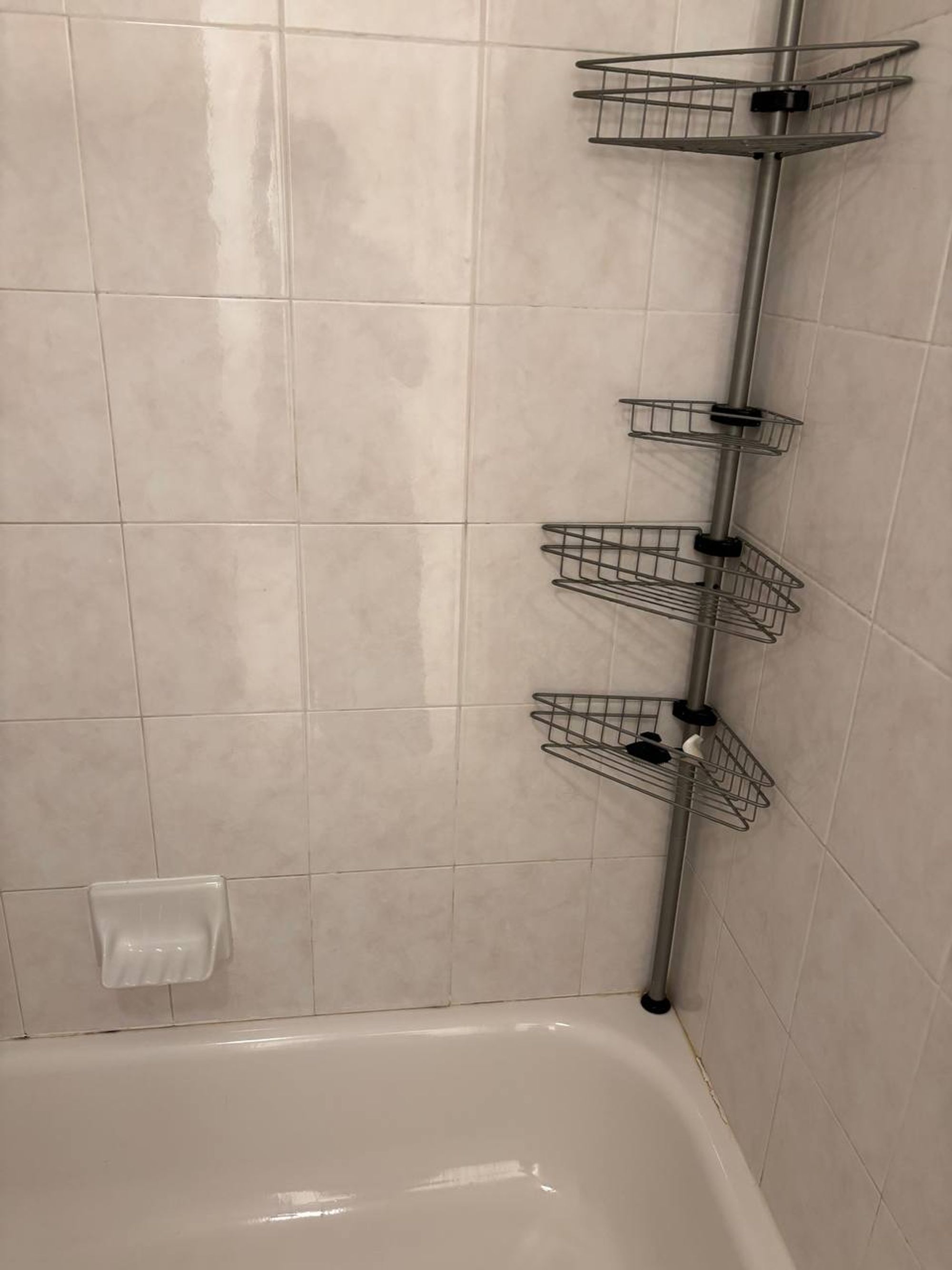White tiled tub wall with chrome corner caddy and soap dish