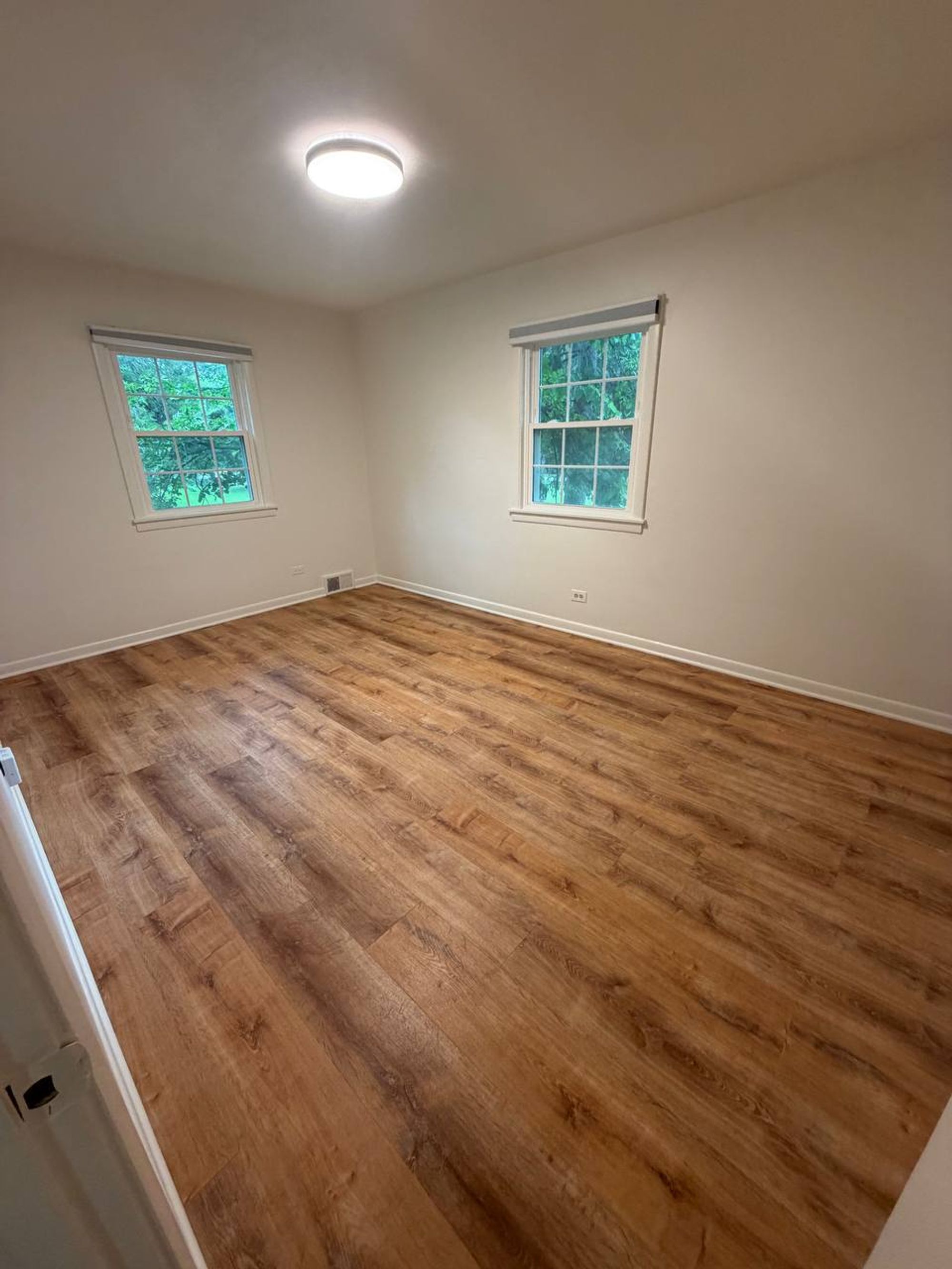 Empty bedroom with two windows and freshly cleaned wood-look floor