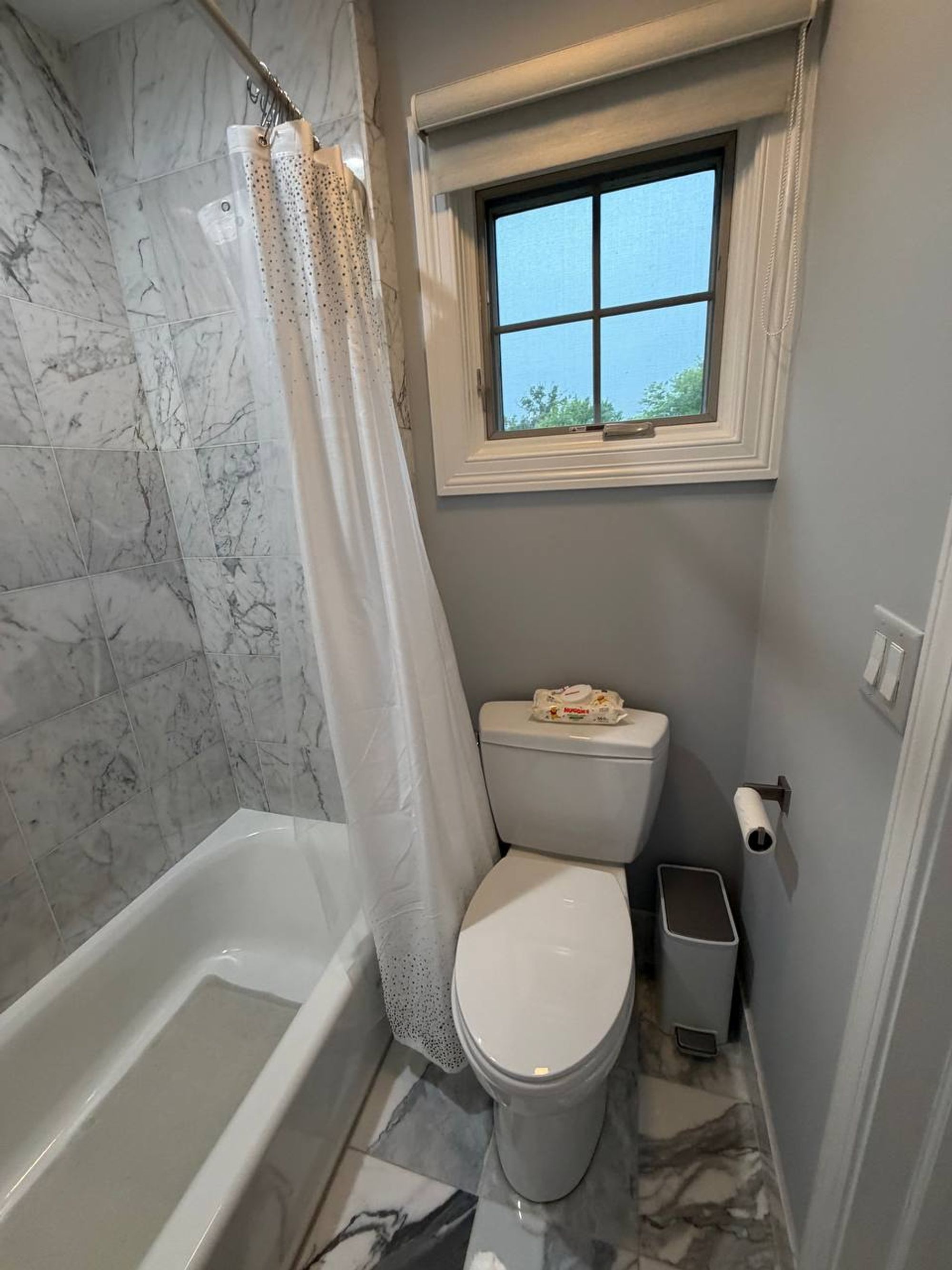 White toilet and tub under a small window in a marble bathroom