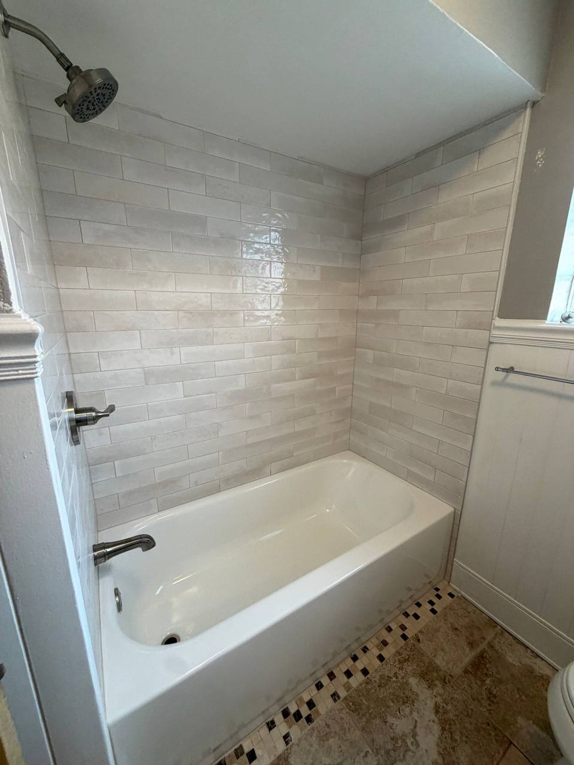 White tub with subway tile wall and mosaic tile border